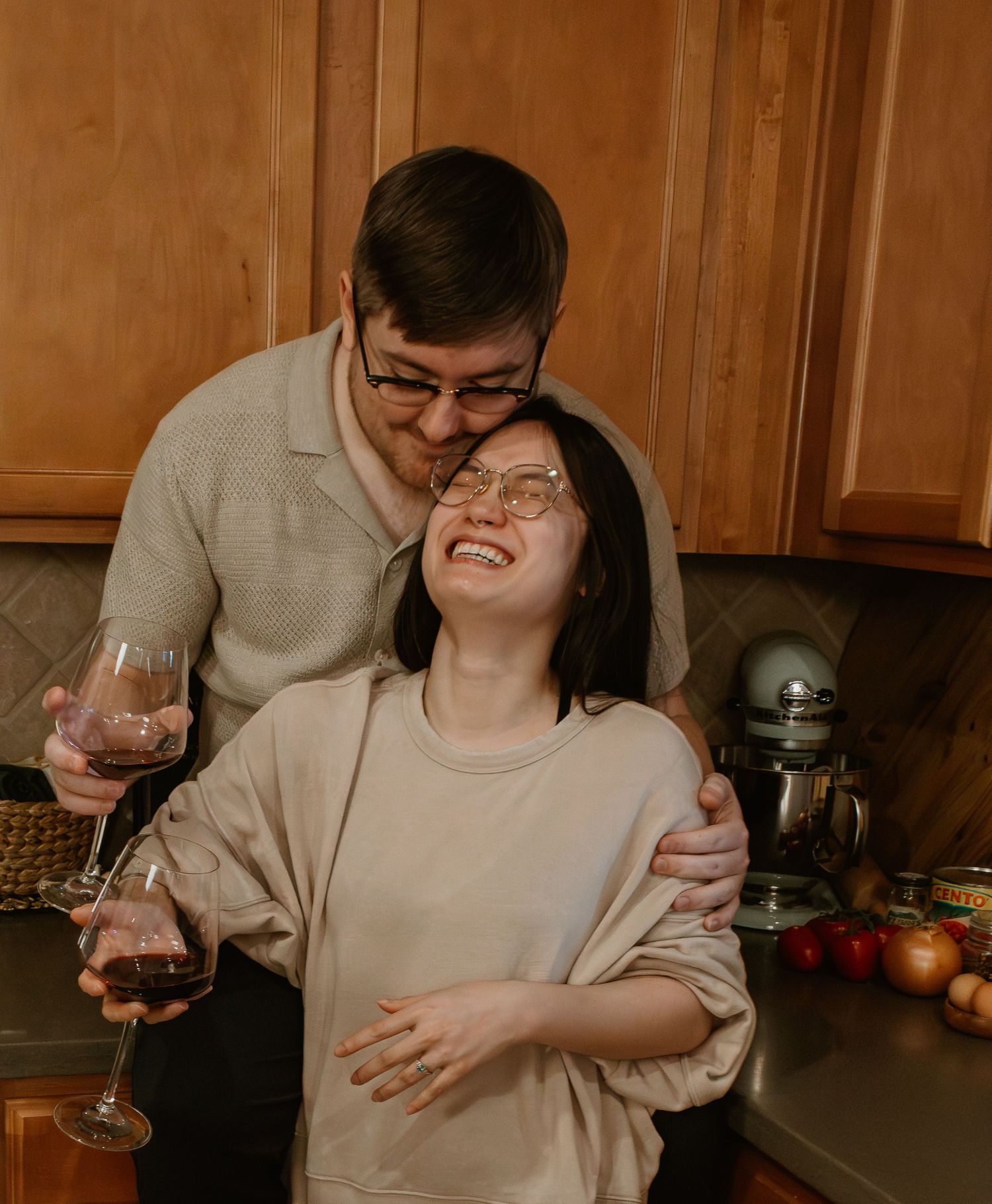 A couple sharing wine and laughing while cooking together in their kitchen.