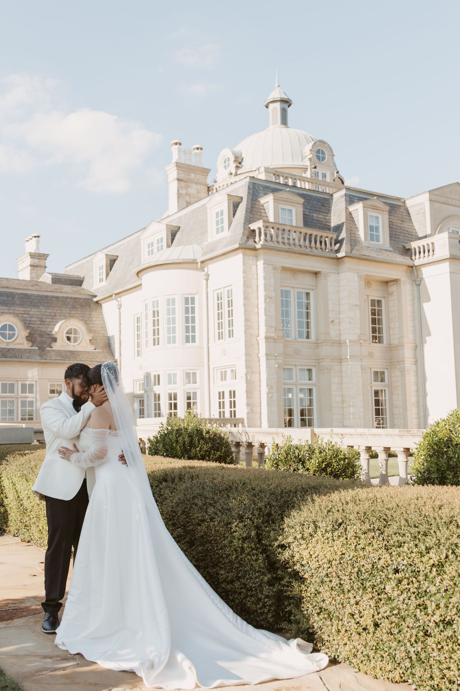 A romantic wedding photoshoot takes place against the backdrop of a stunning French chateau with manicured hedges.