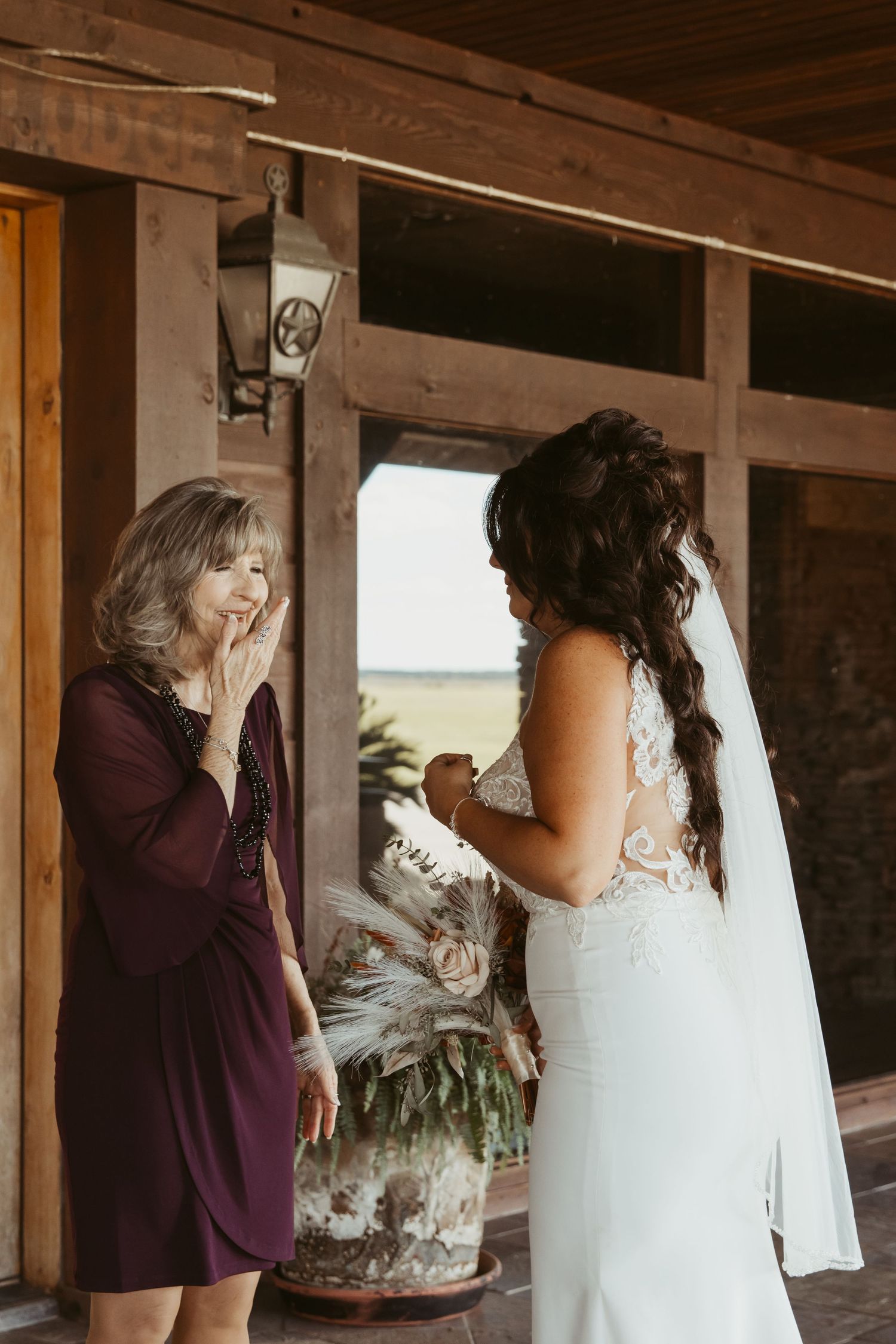 A touching scene with a bride in white being embraced by someone wearing purple in a rustic indoor setting. Wedding photographer DFW