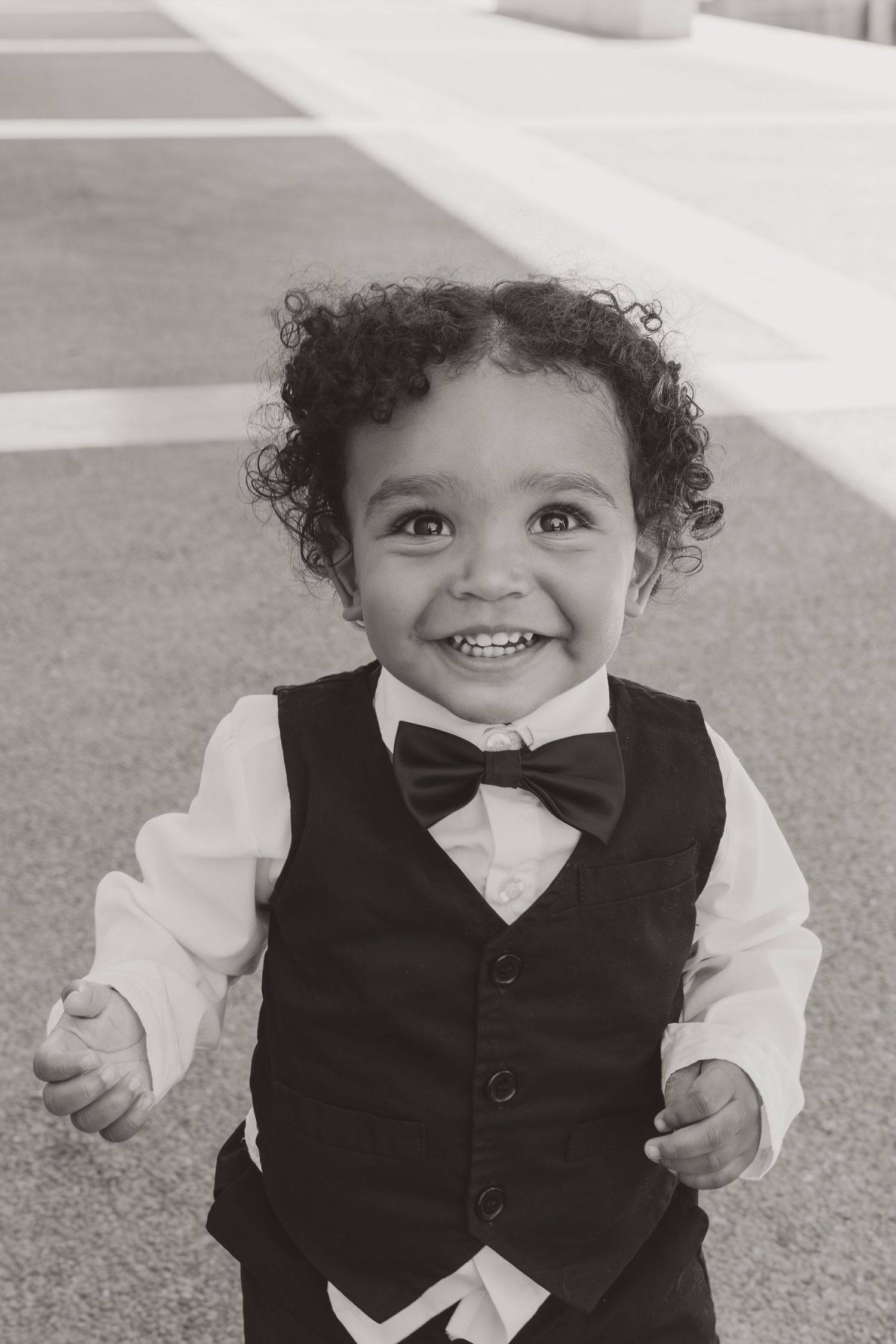 A small child in formal attire smiling with joy in black and white photography. Wedding Photographer DFW