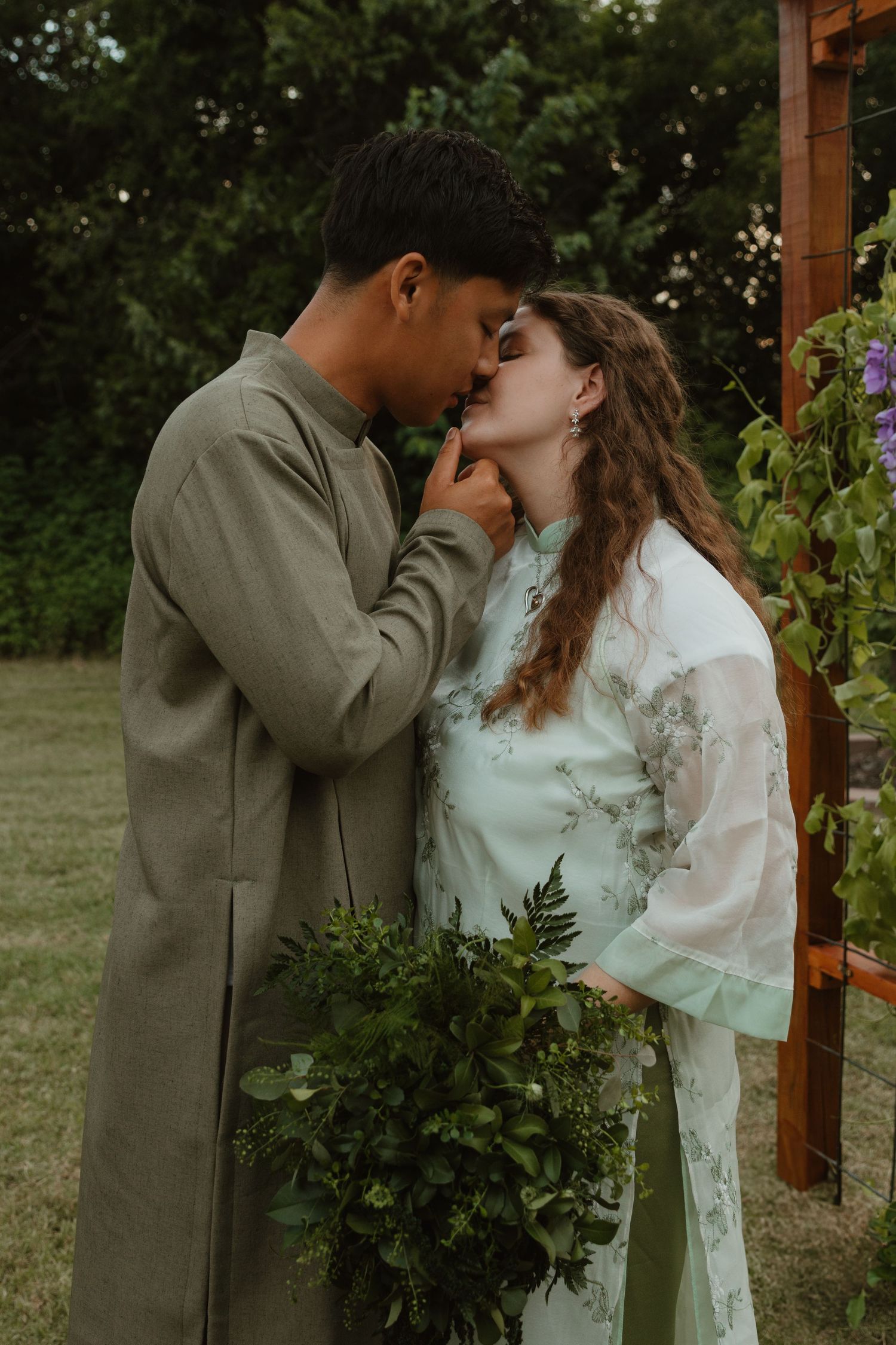 A romantic moment between a couple in wedding attire near a garden trellis.