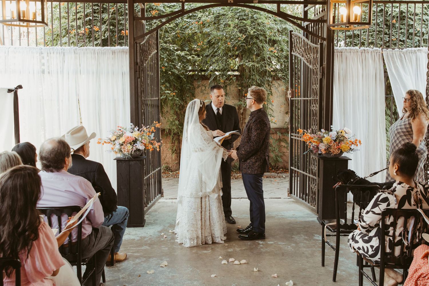 An intimate wedding ceremony under an iron arch with white draping and floral decorations.