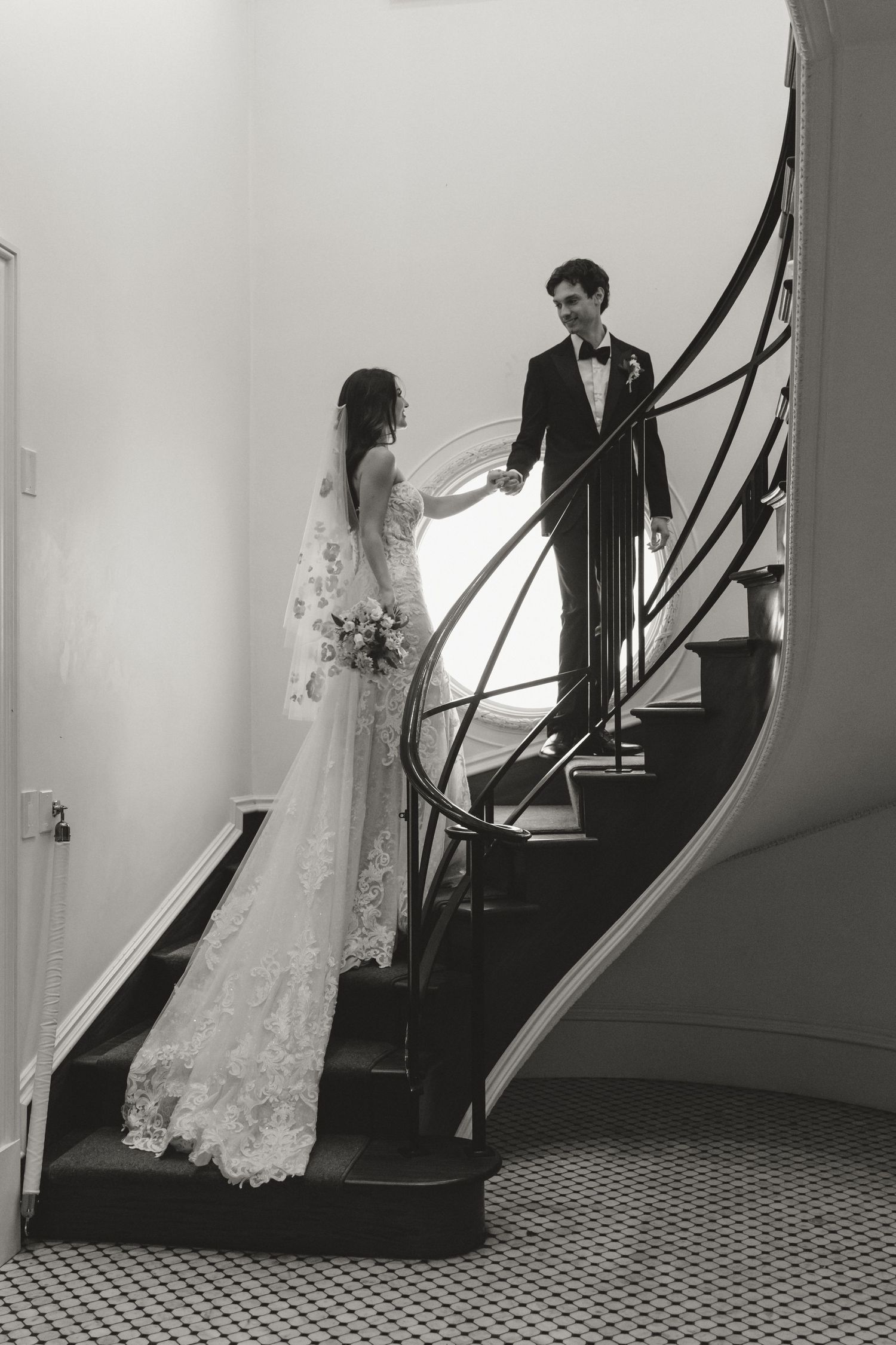 Black and white wedding photos on a classic staircase with patterned carpet and dramatic lighting.