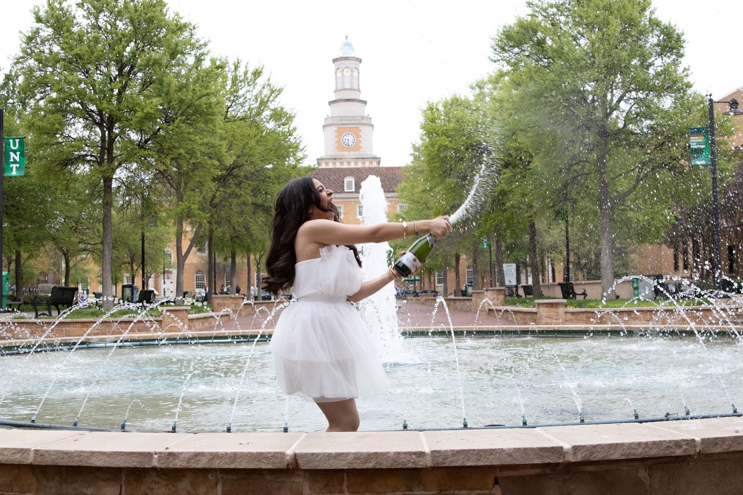 A celebratory pose captured in front of a campus fountain with a clock tower in the background.
