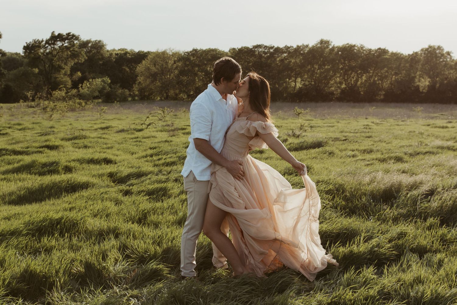 Romantic couple sits together in a sunlit meadow during golden hour, creating an intimate moment in nature.