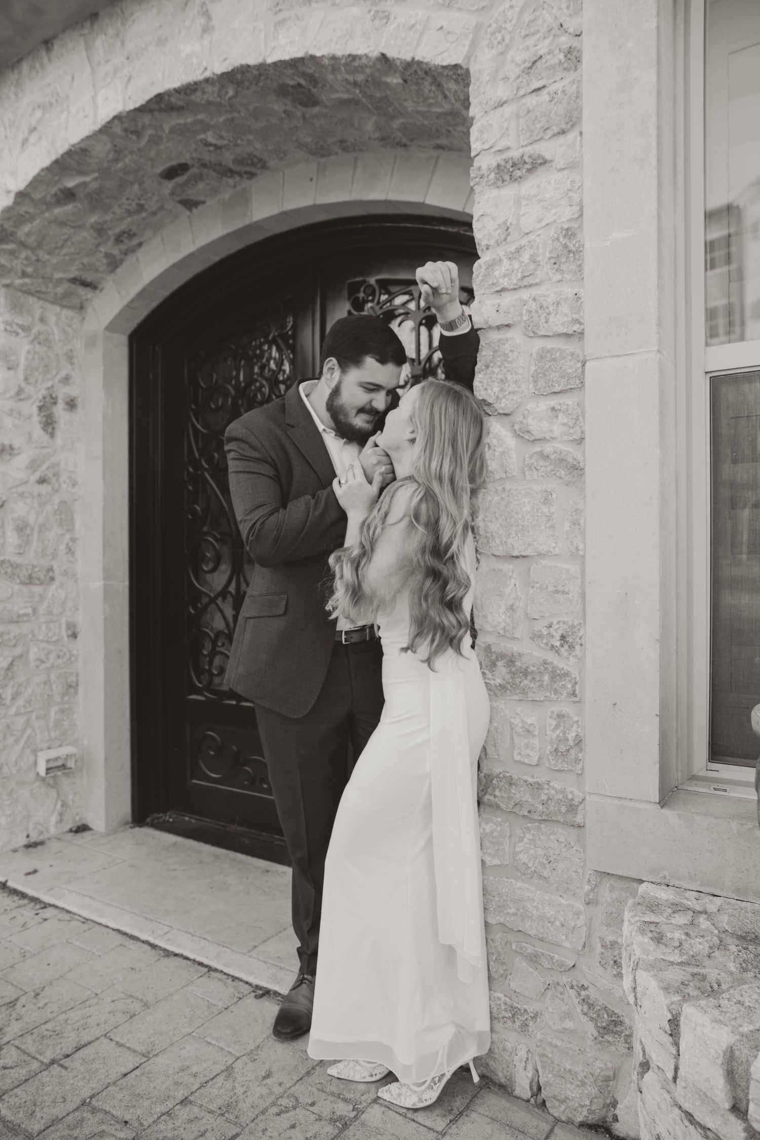 A couple shares an intimate moment against a weathered stone wall with arched doorways.