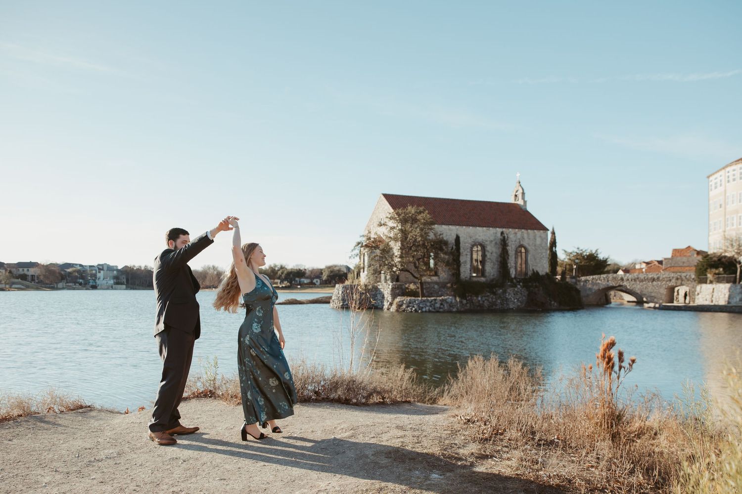 Wedding party enjoys playful moments along a waterfront promenade with church and harbor in background.