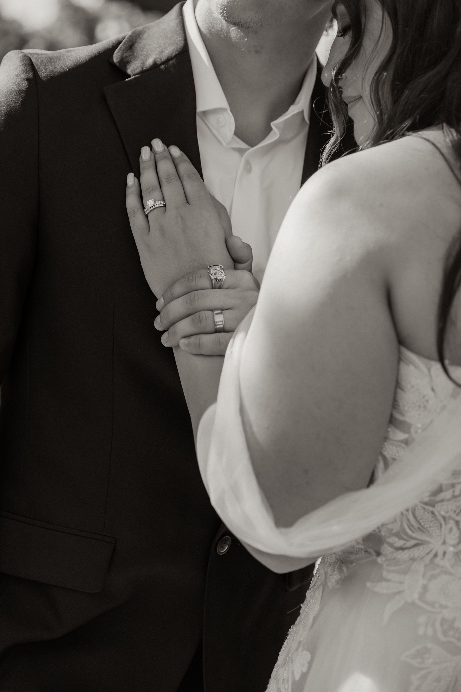 Black and white photo of bride and groom embracing, showcasing wedding rings on the bride's hand.