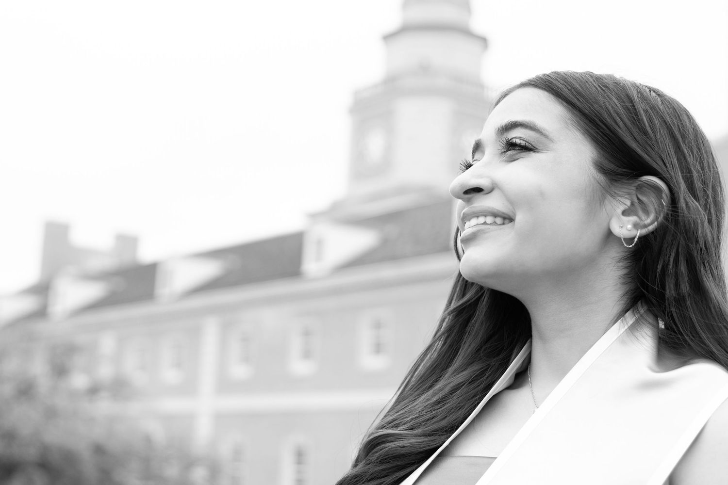 Black and white portrait photo showing someone smiling with eyes closed against a blurred architectural background.