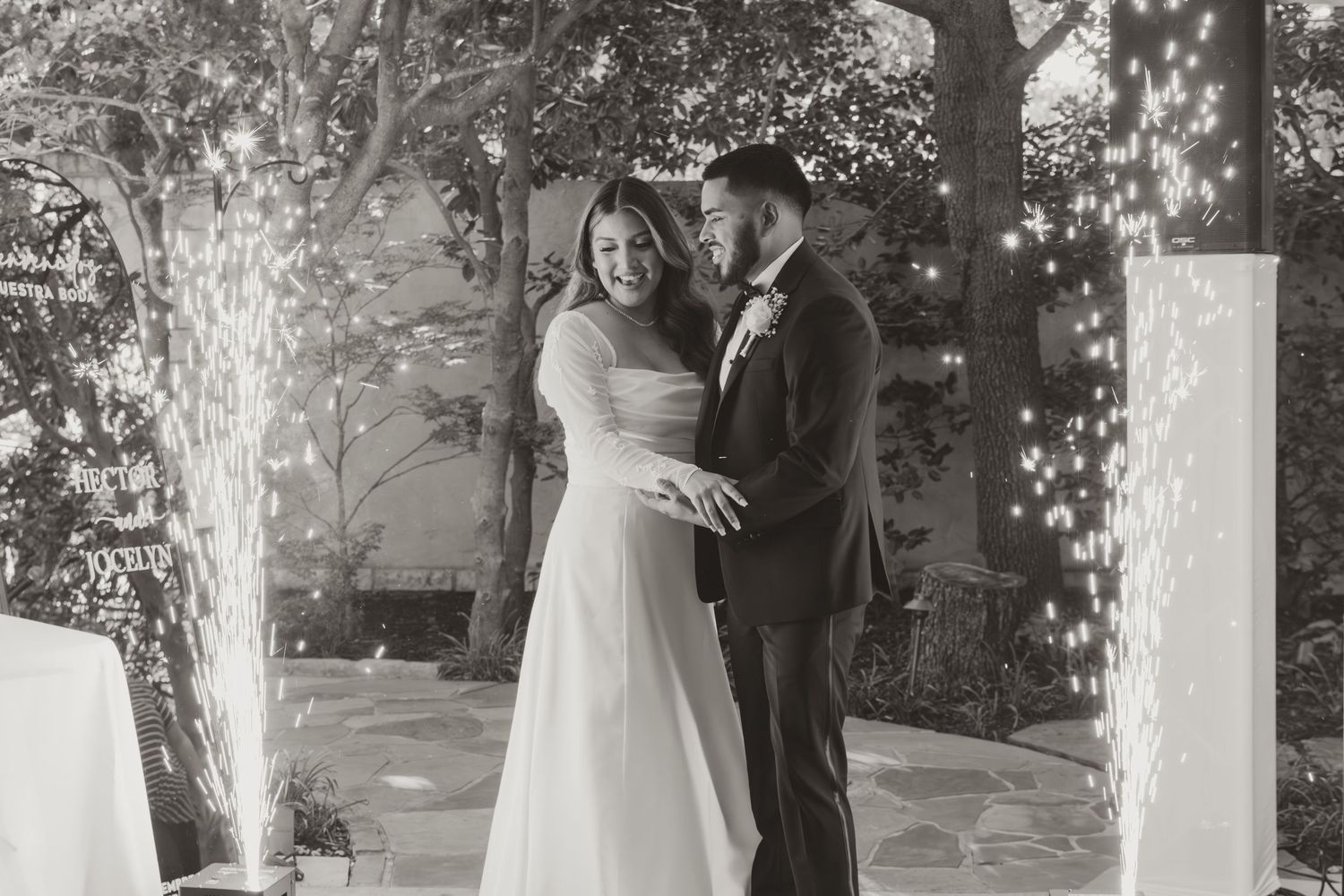 Wedding ceremony moment captured outdoors with bright sunlight filtering through trees and white decor elements.