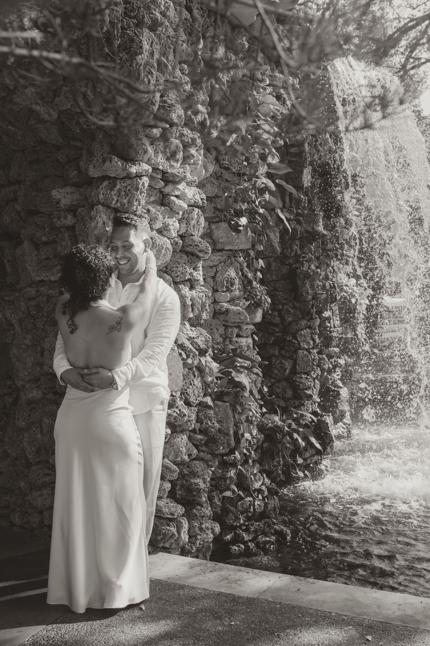 A romantic series of photos in a stone garden walkway showing a couple in white embracing against rustic walls.