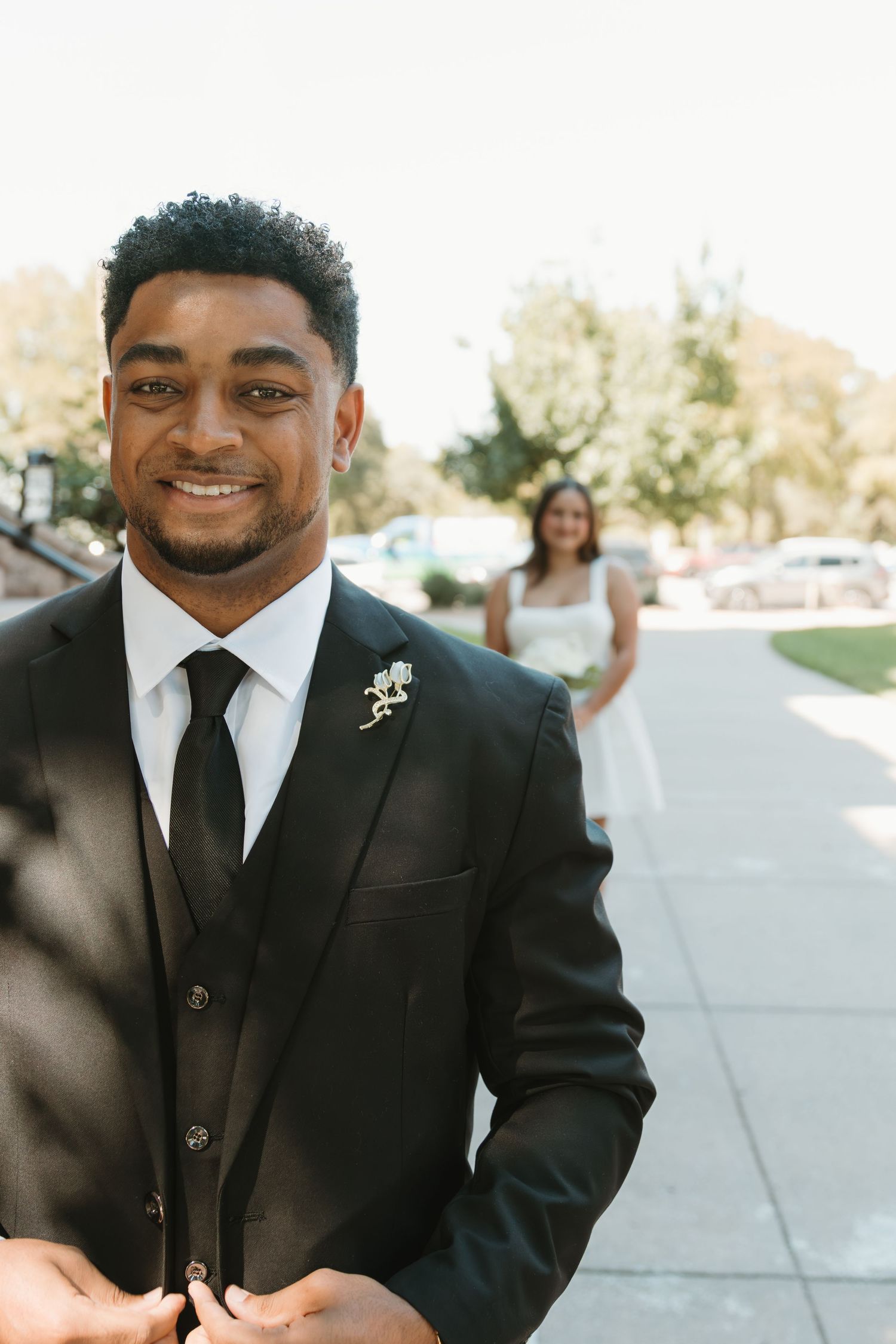 Groom in classic black tuxedo and tie smiles warmly on his wedding day outdoors. Wedding Photographer DFW