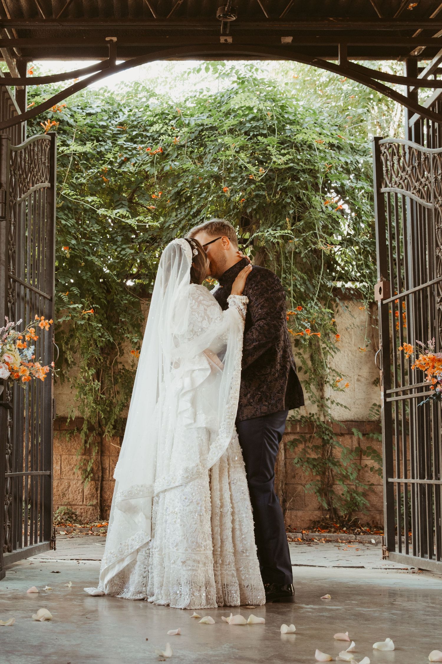Wedding party gathered in a covered outdoor space with ornate iron gates and greenery.