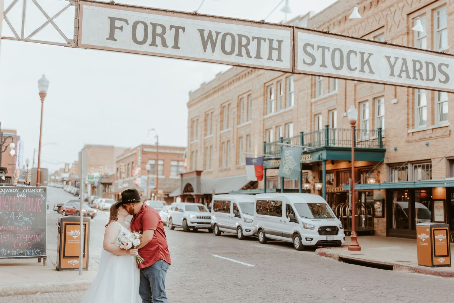 A couple shares a romantic moment under the Fort Worth Stock Yards sign on a cloudy day.