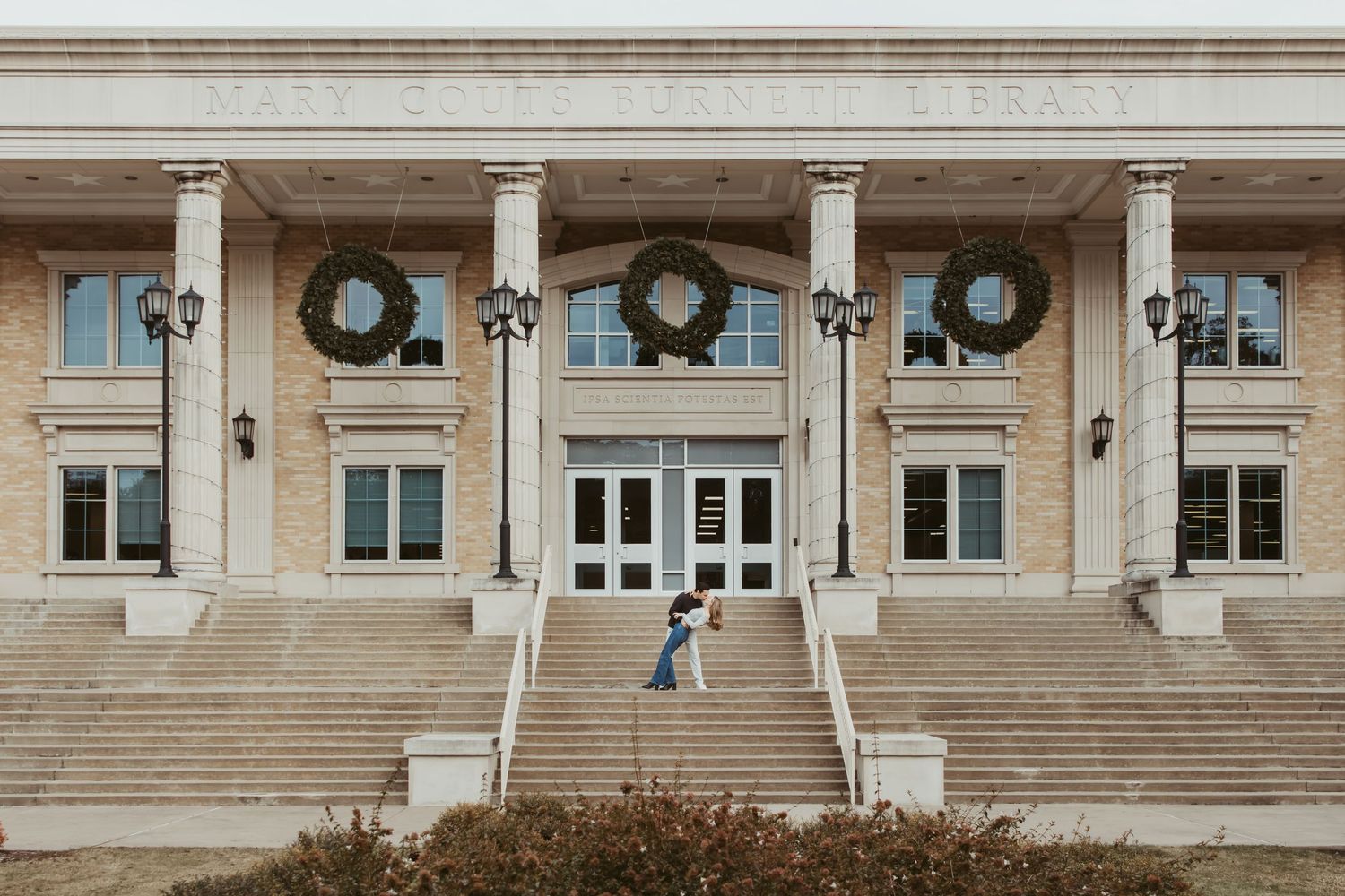 Stone building entrance with three holiday wreaths hanging above double doors and symmetrical staircases leading to entrance. Wedding photog