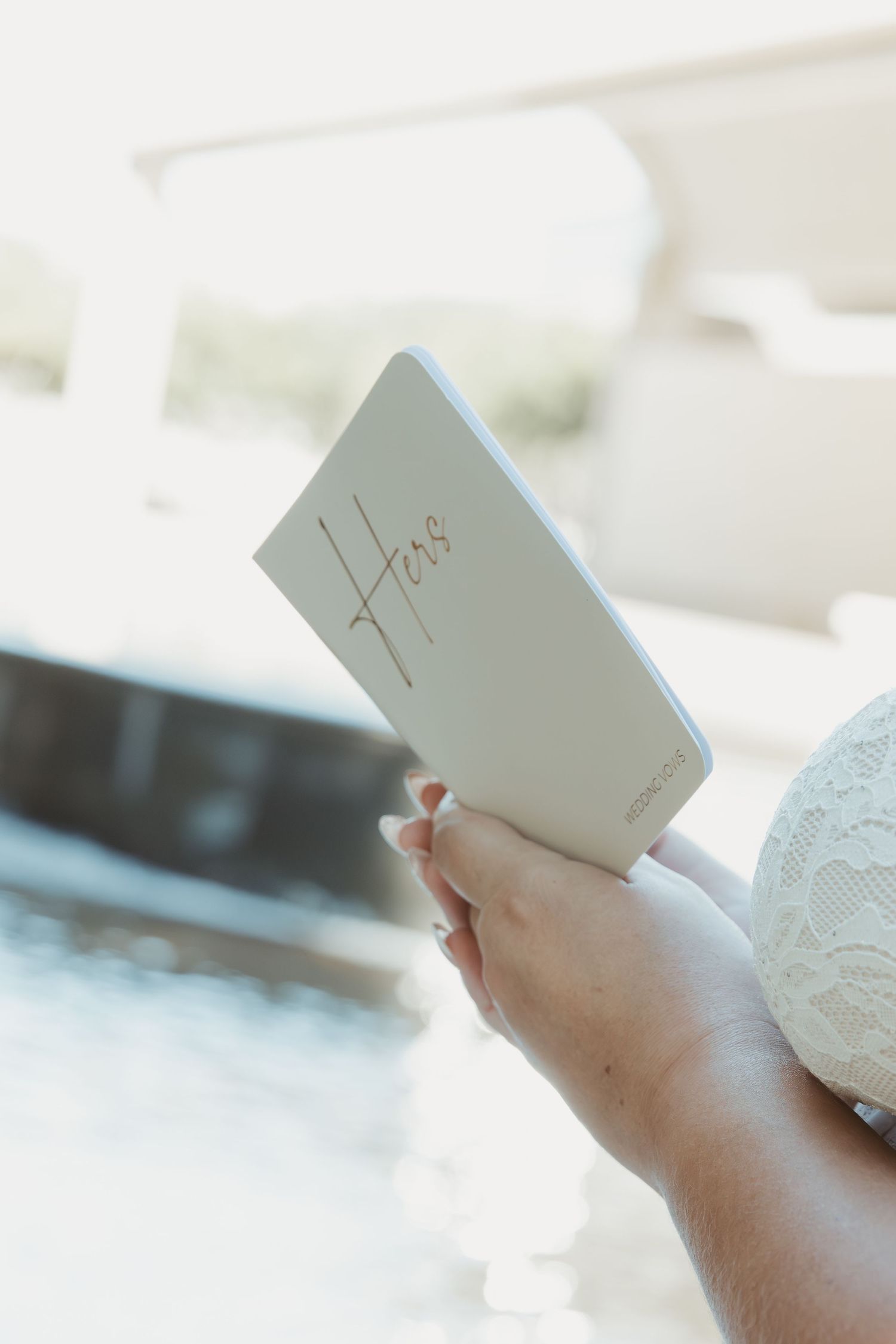 Hands holding a white card or invitation with delicate lace details in soft natural lighting. Wedding Photographer DFW