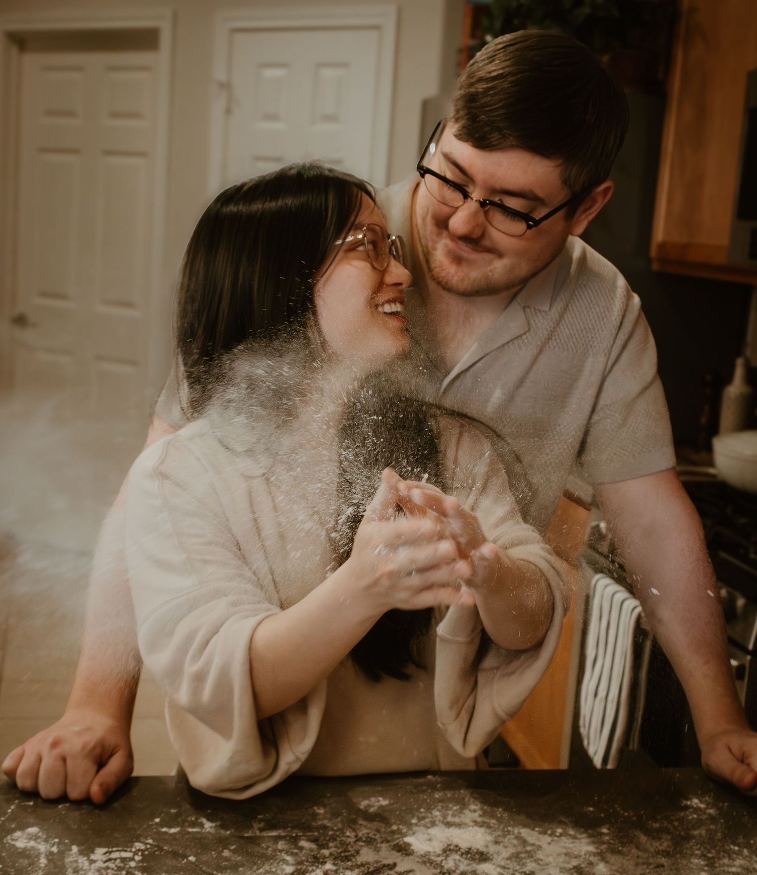 A couple laughs together while preparing food in their kitchen.