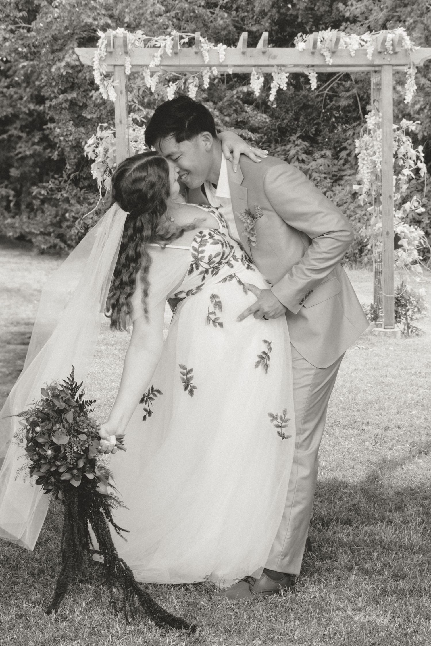 A romantic black and white wedding photo of a couple under a decorated arbor.
