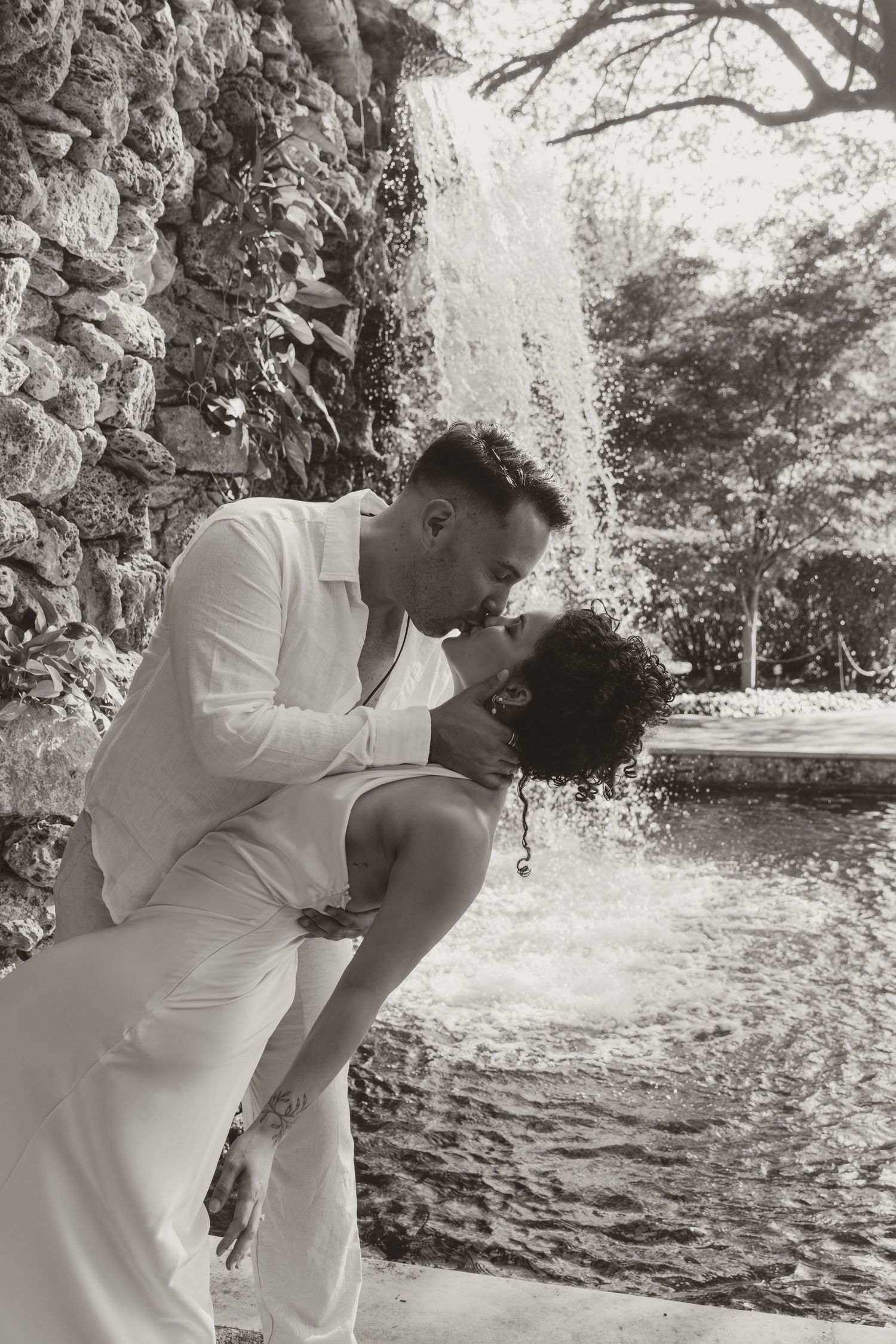 A romantic black and white photo sequence of a couple sharing an intimate kiss in an outdoor garden setting.