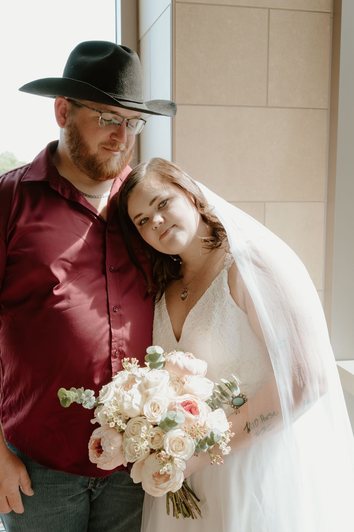 A rustic wedding couple poses together with a beautiful bouquet of pink and white roses.