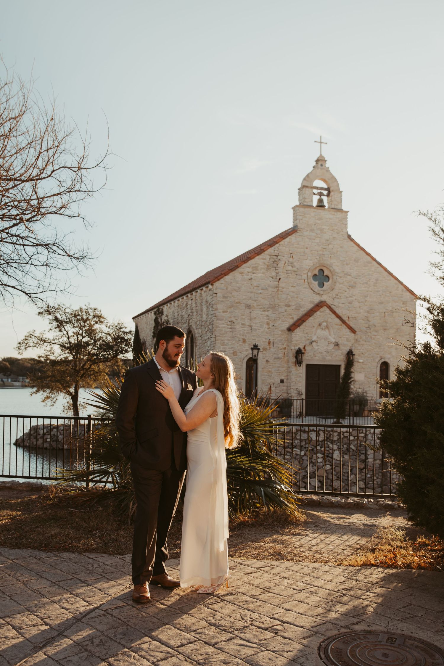 A couple shares a romantic moment outside a rustic stone church during sunset.