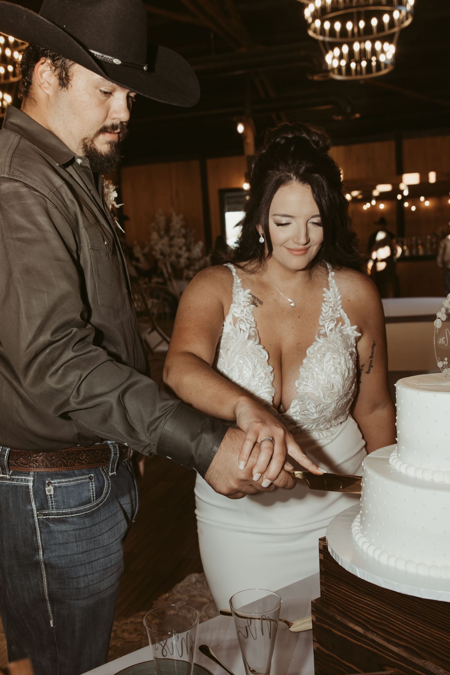 Wedding cake cutting sequence showing detailed white tiered cake and western-style attire. Wedding photographer DFW