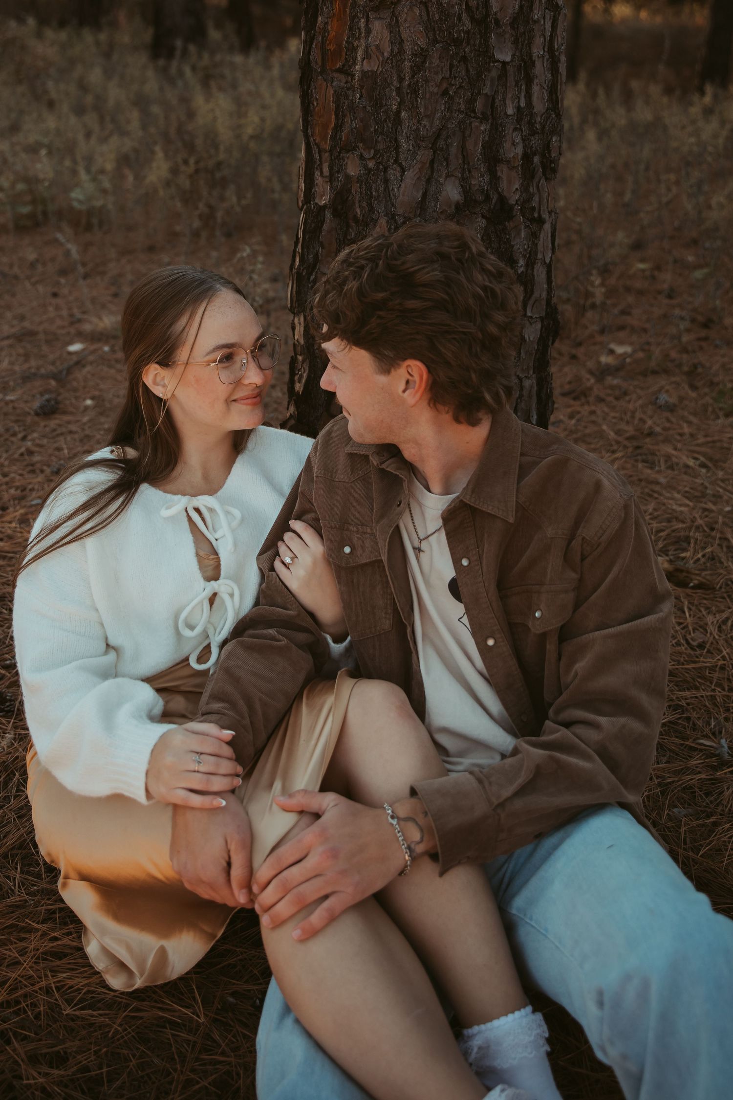 Couple in casual attire sharing tender moments while sitting in a pine forest. engagement photos Fort Worth