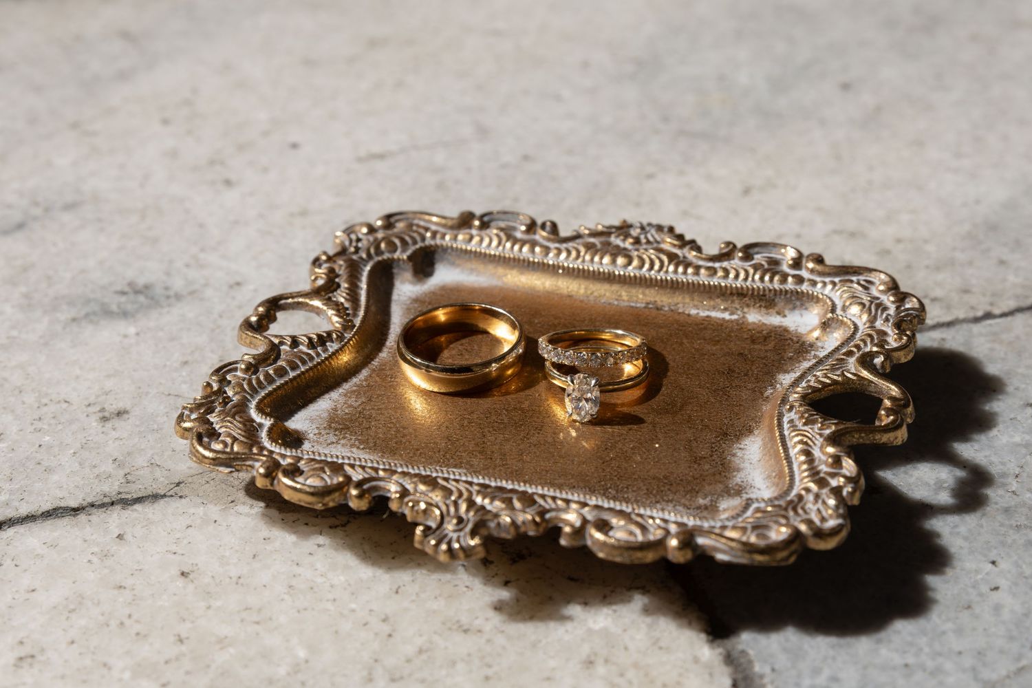 Wedding rings displayed on an ornate vintage silver tray with decorative scrollwork edges.