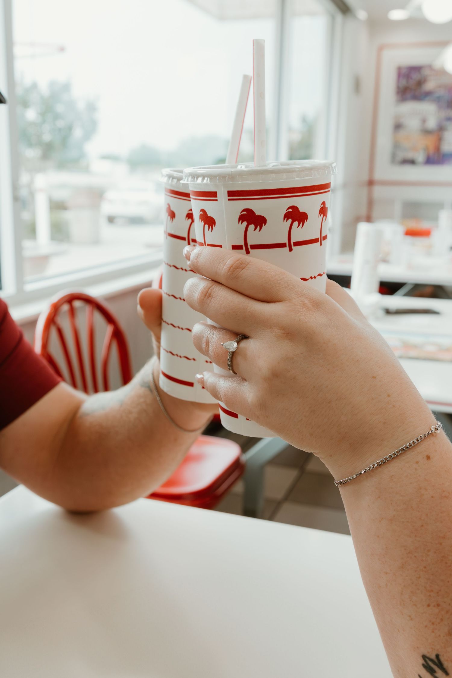 In-N-Out drink cup with palm tree logo held against bright window.