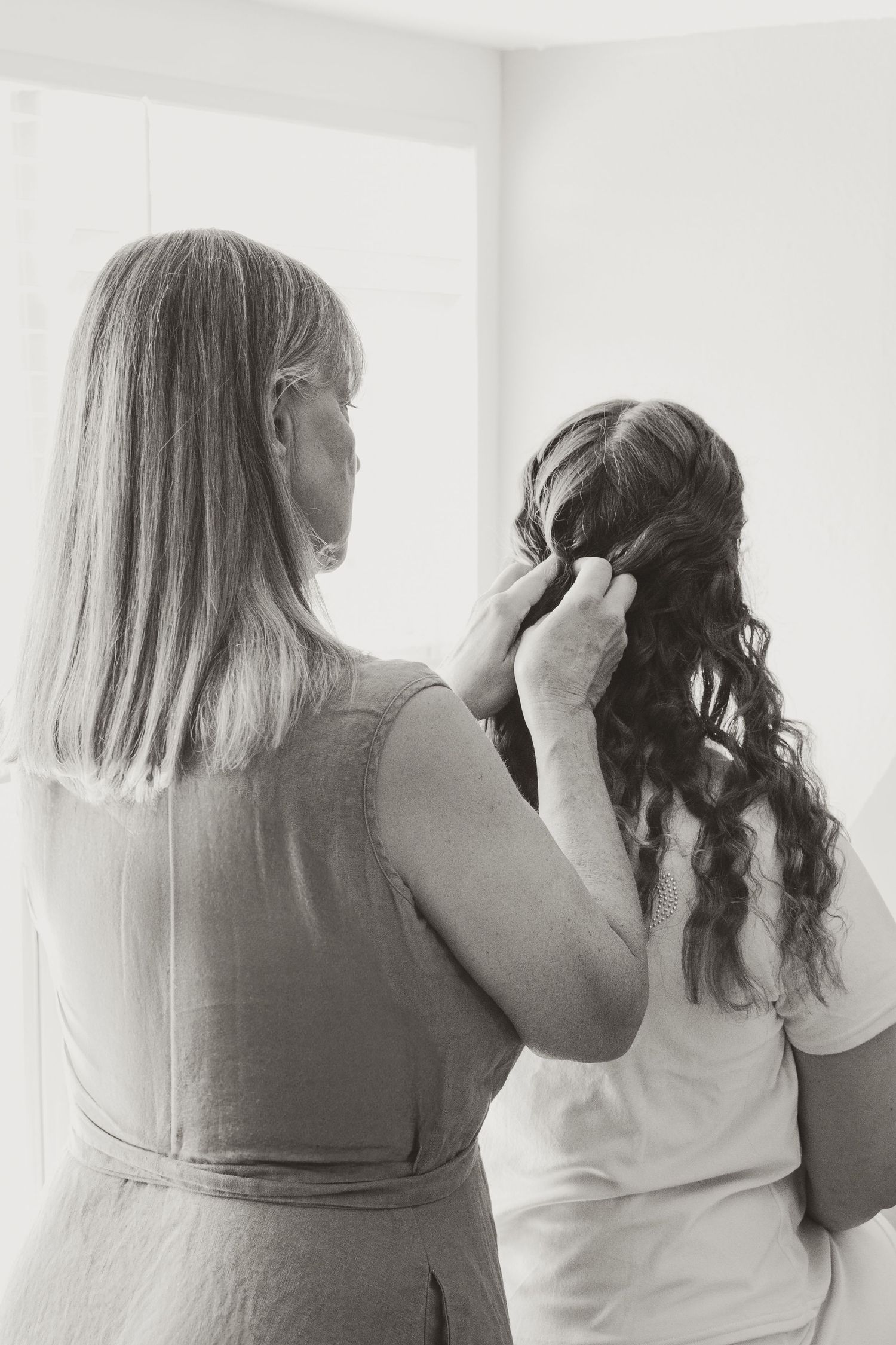 Black and white photo capturing an intimate hair styling moment during wedding preparations.