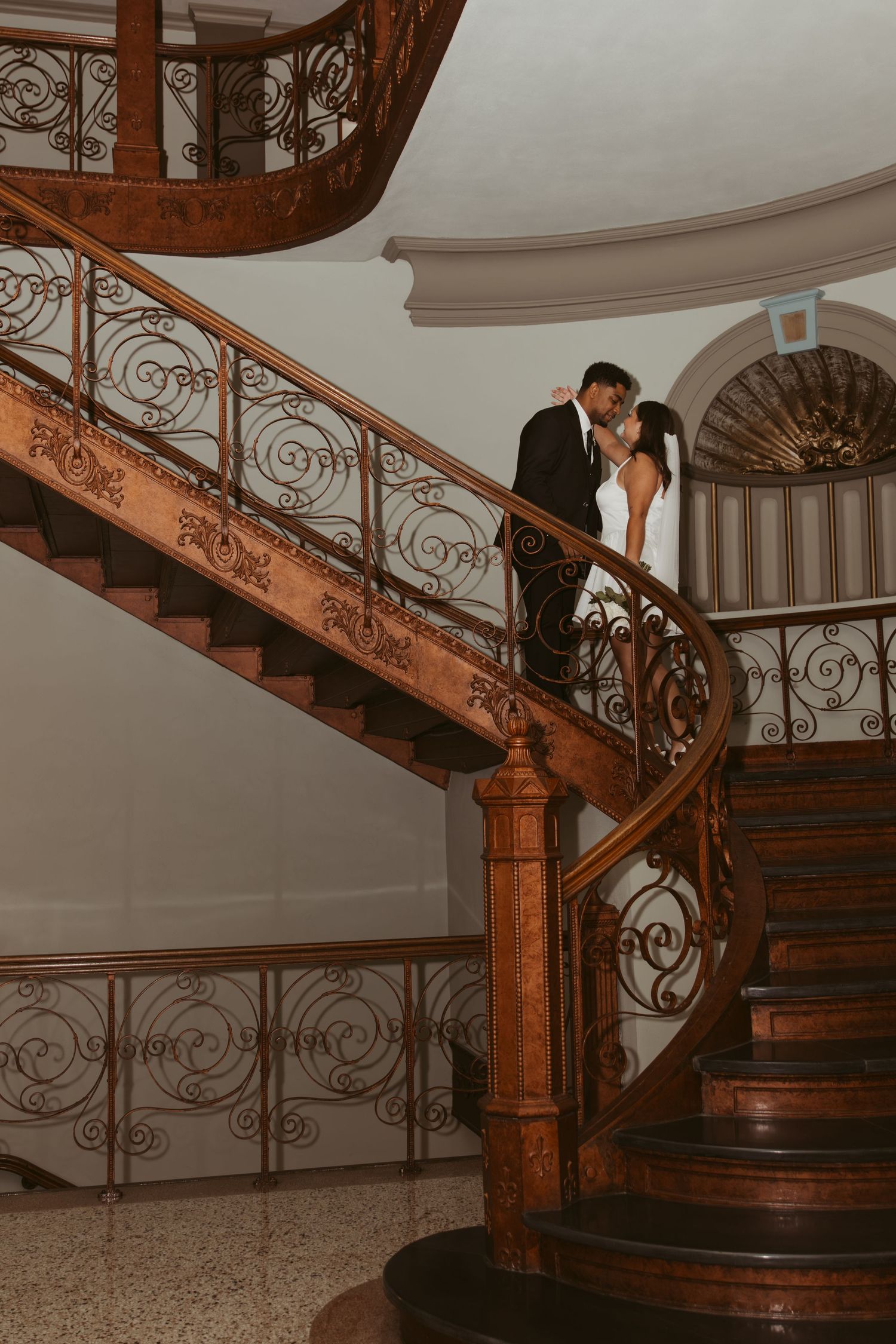 An ornate wooden staircase with intricate iron railings in a grand interior setting. Wedding Photographer DFW