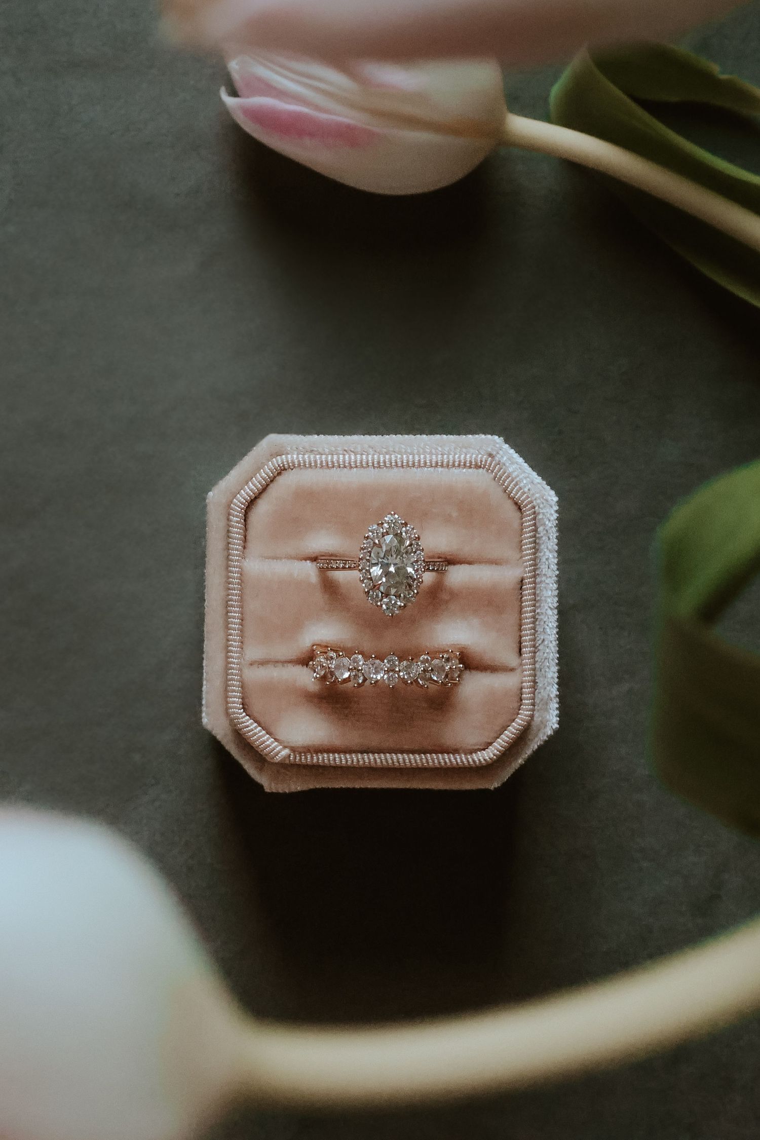 Two diamond engagement rings nestled in a blush pink velvet ring box with a tulip flower in the background.