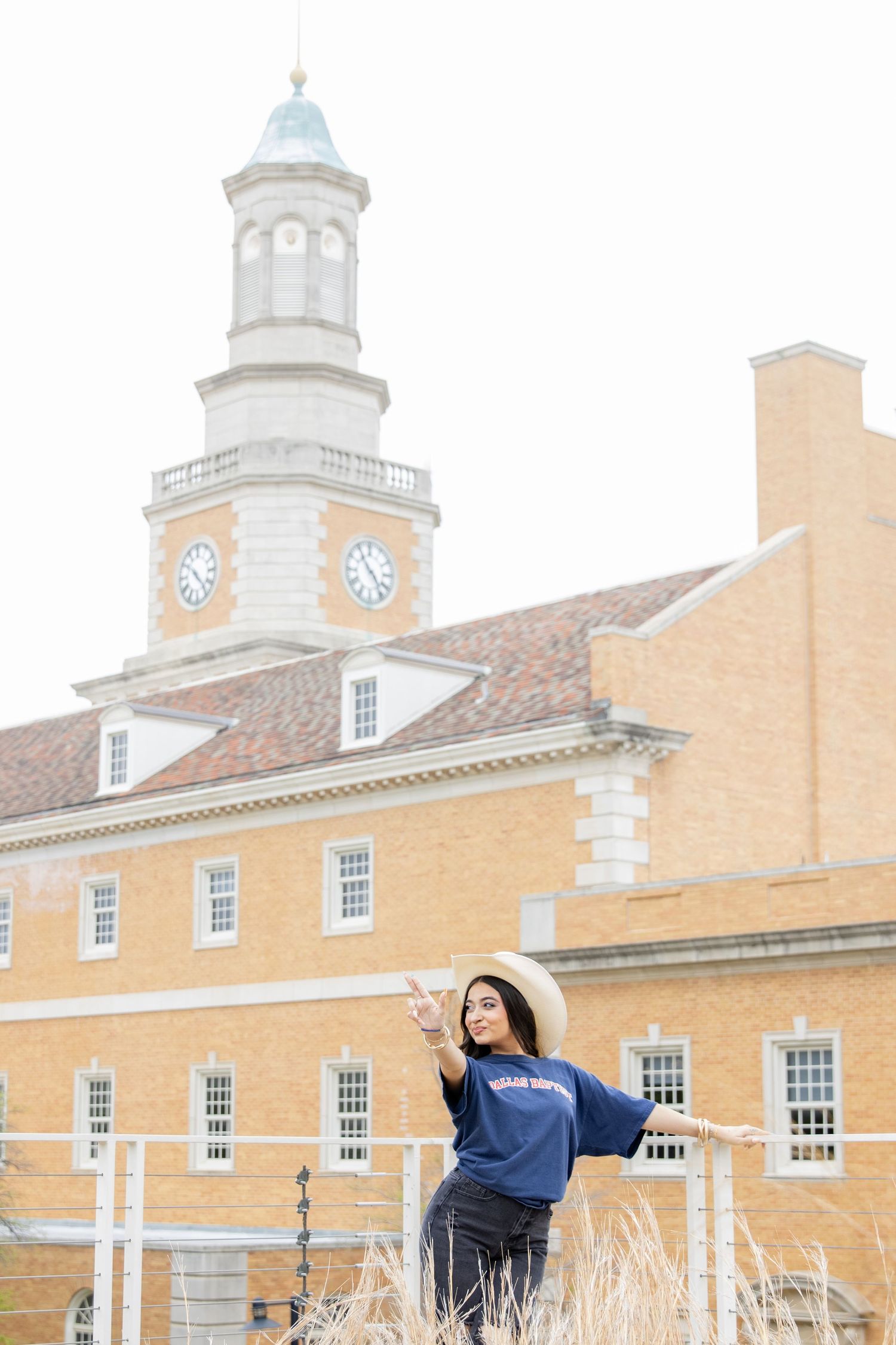 Person in navy sweatshirt poses joyfully in front of traditional college building with white clock tower.