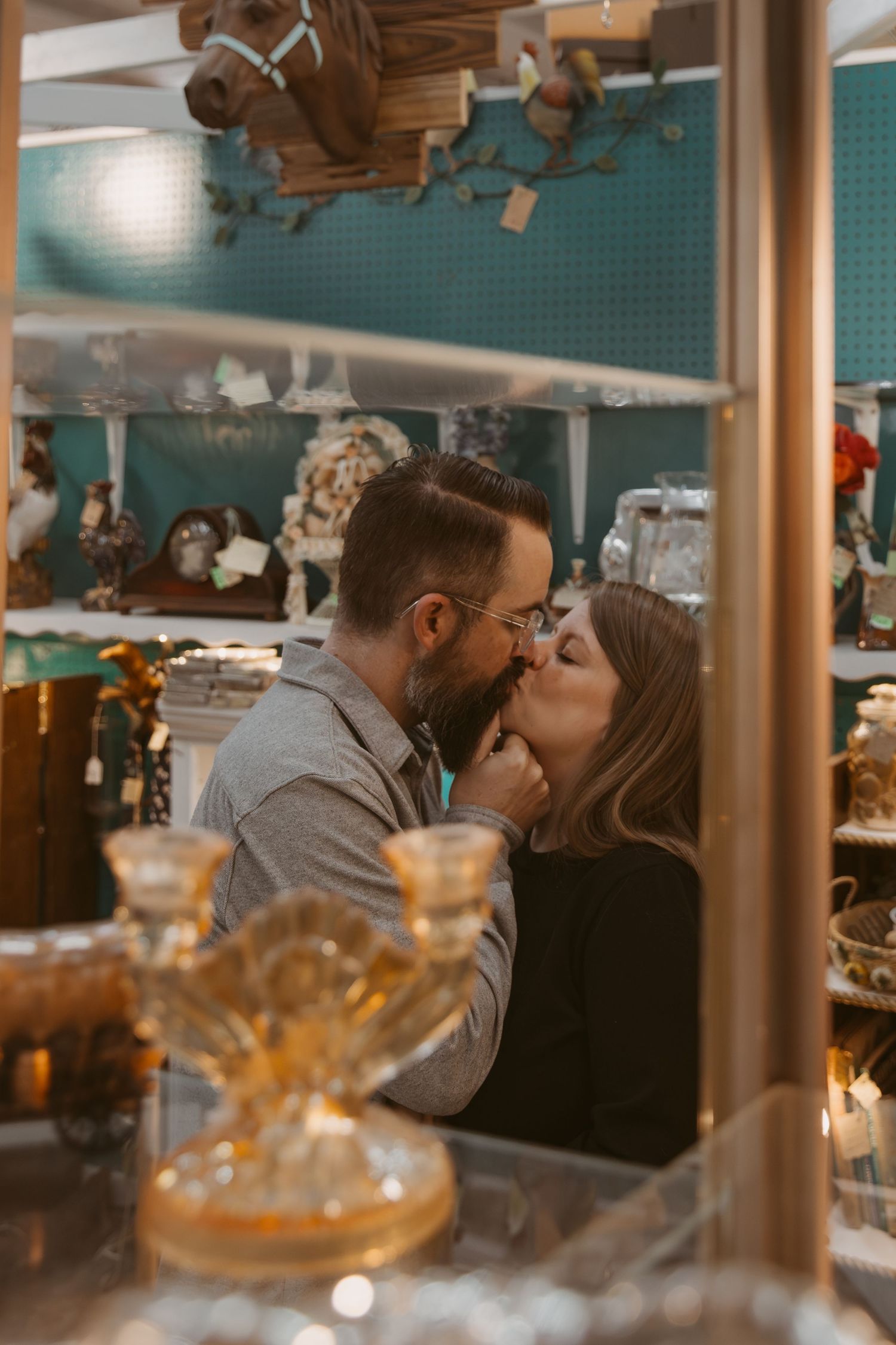 A romantic couple shares an intimate kiss at a cozy restaurant with warm lighting and blurred decor in the background.