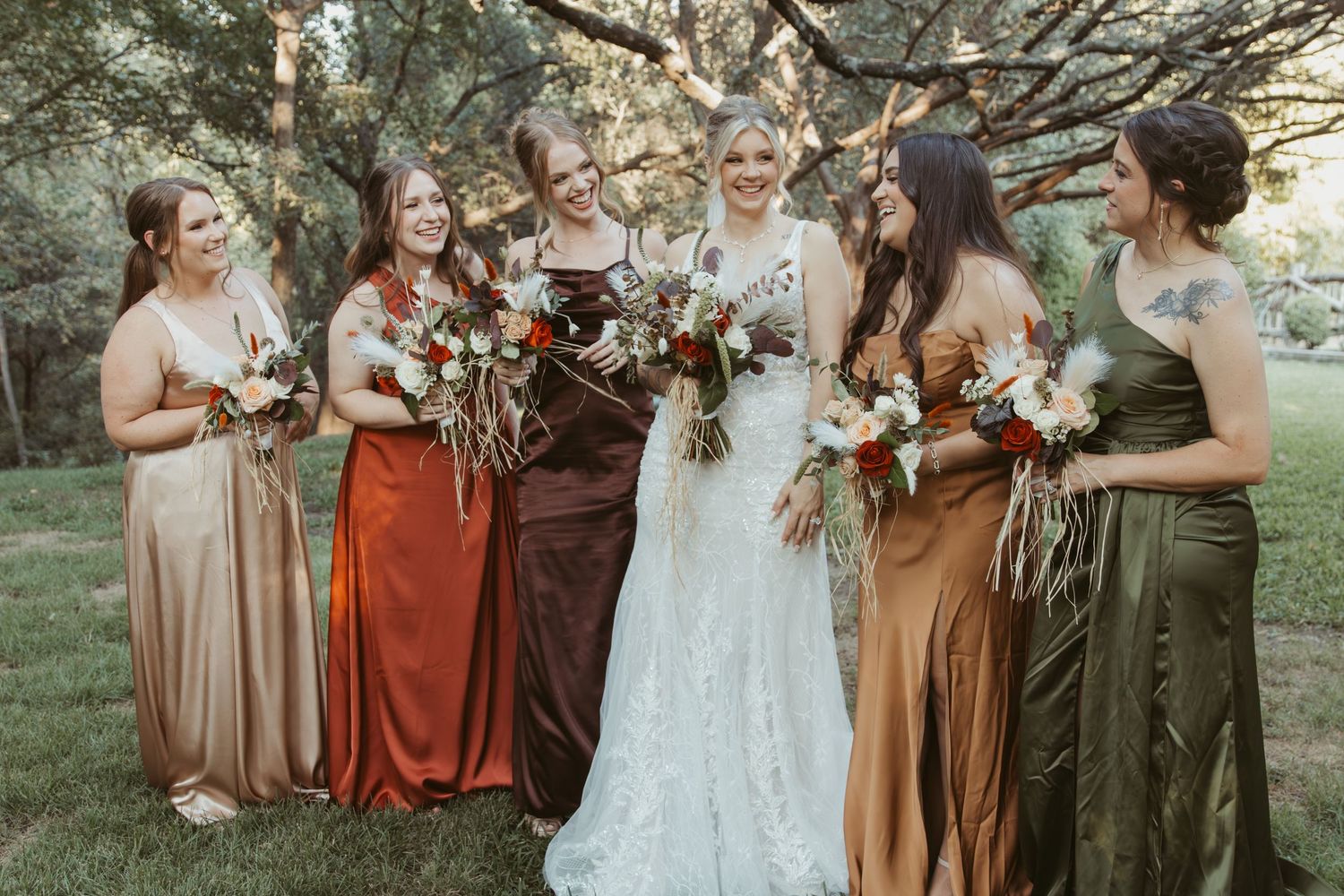 Wedding party in earth-toned dresses poses together outdoors in a natural setting during autumn. Wedding Photographer DFW