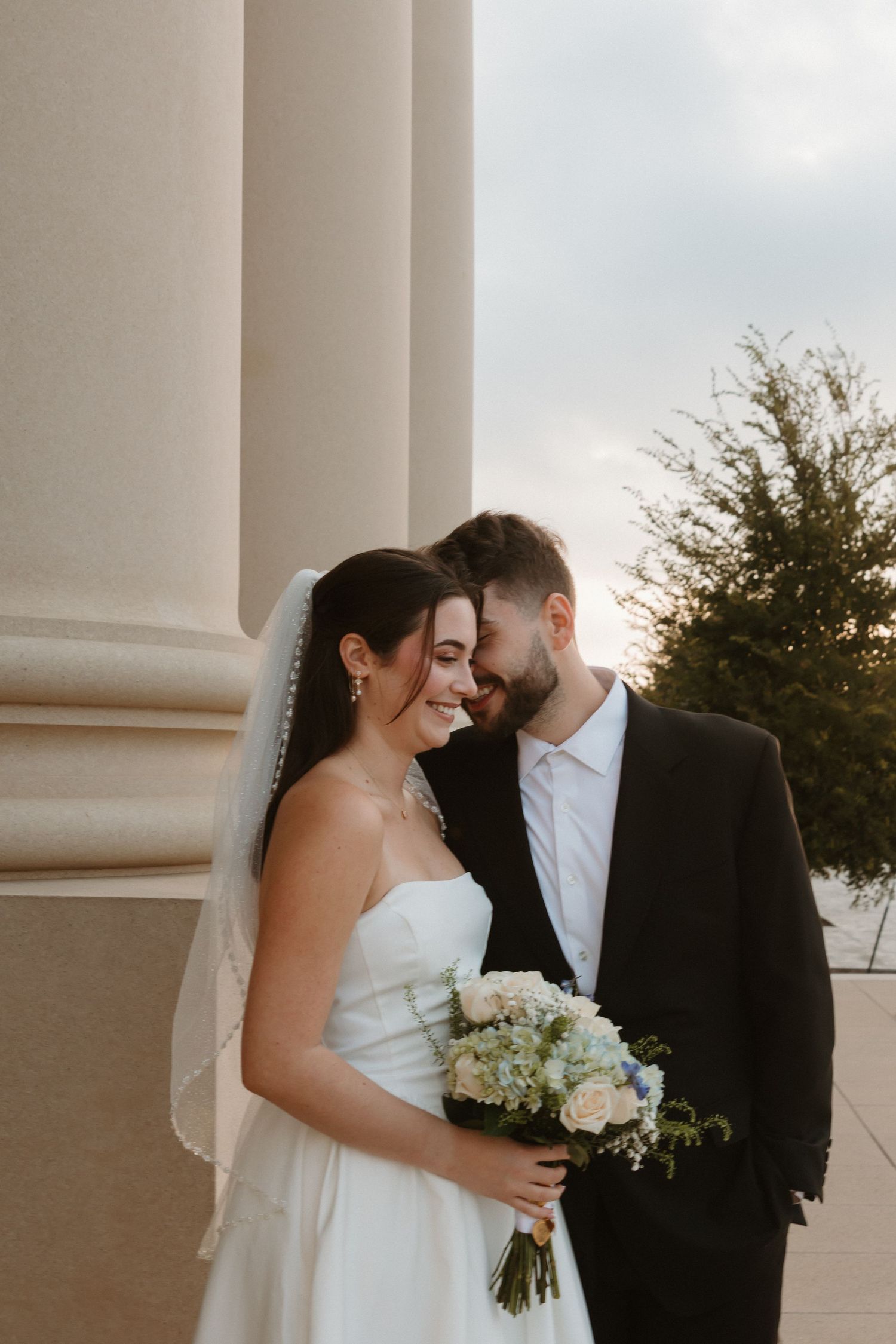 A romantic wedding couple shares an intimate moment between elegant white columns during their photo session Wedding Photographer Fort Worth
