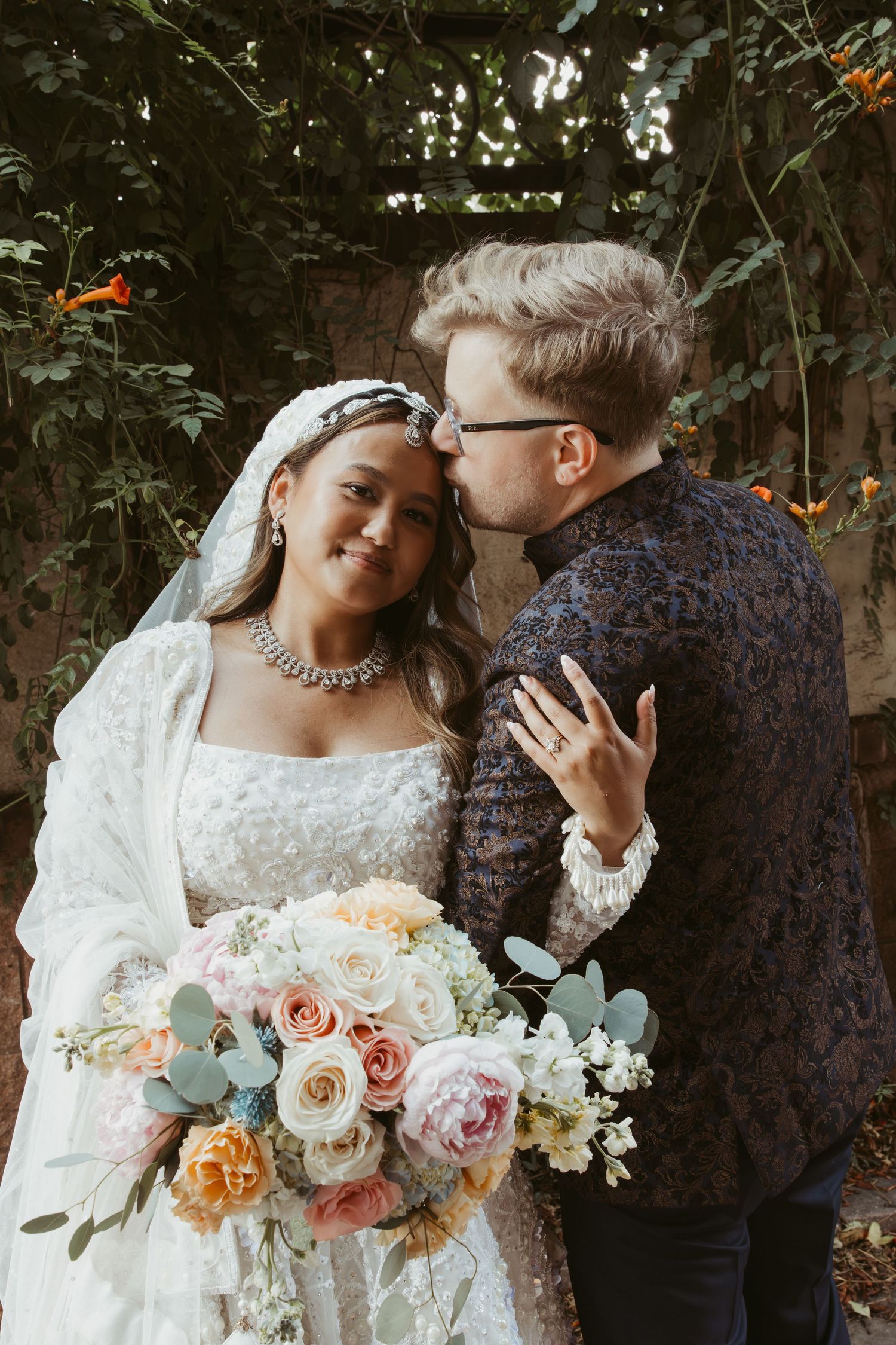 A romantic wedding photoshoot featuring a couple with a stunning pastel floral bouquet in an outdoor garden setting.