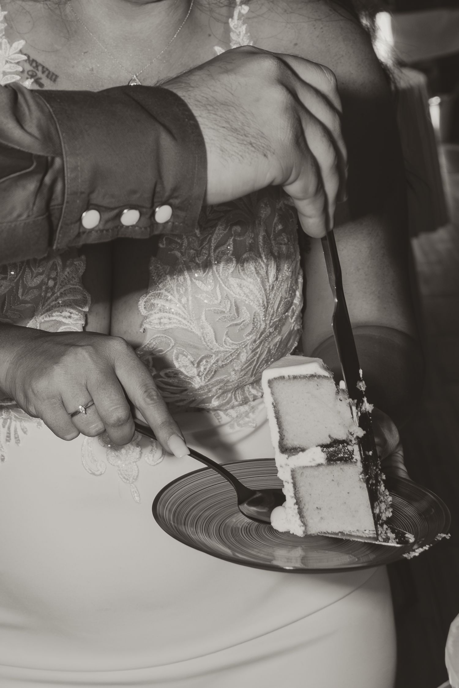 Black and white photograph of hands cutting a slice of wedding cake at a formal reception.
