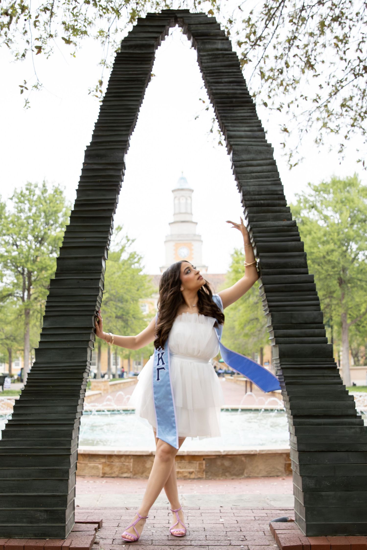 UNT arch sculpture framing the campus admin building with trees and fountain in background.
