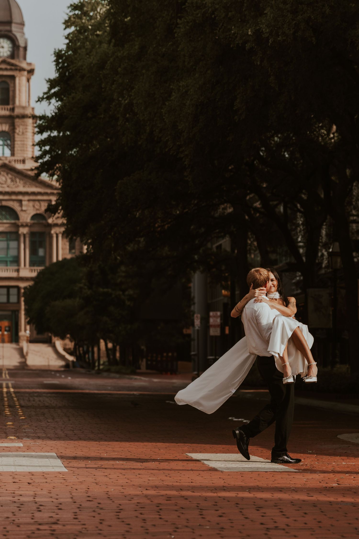 A romantic scene on a cobblestone street shows a couple embracing in a dramatic spin against a historic building backdrop.
