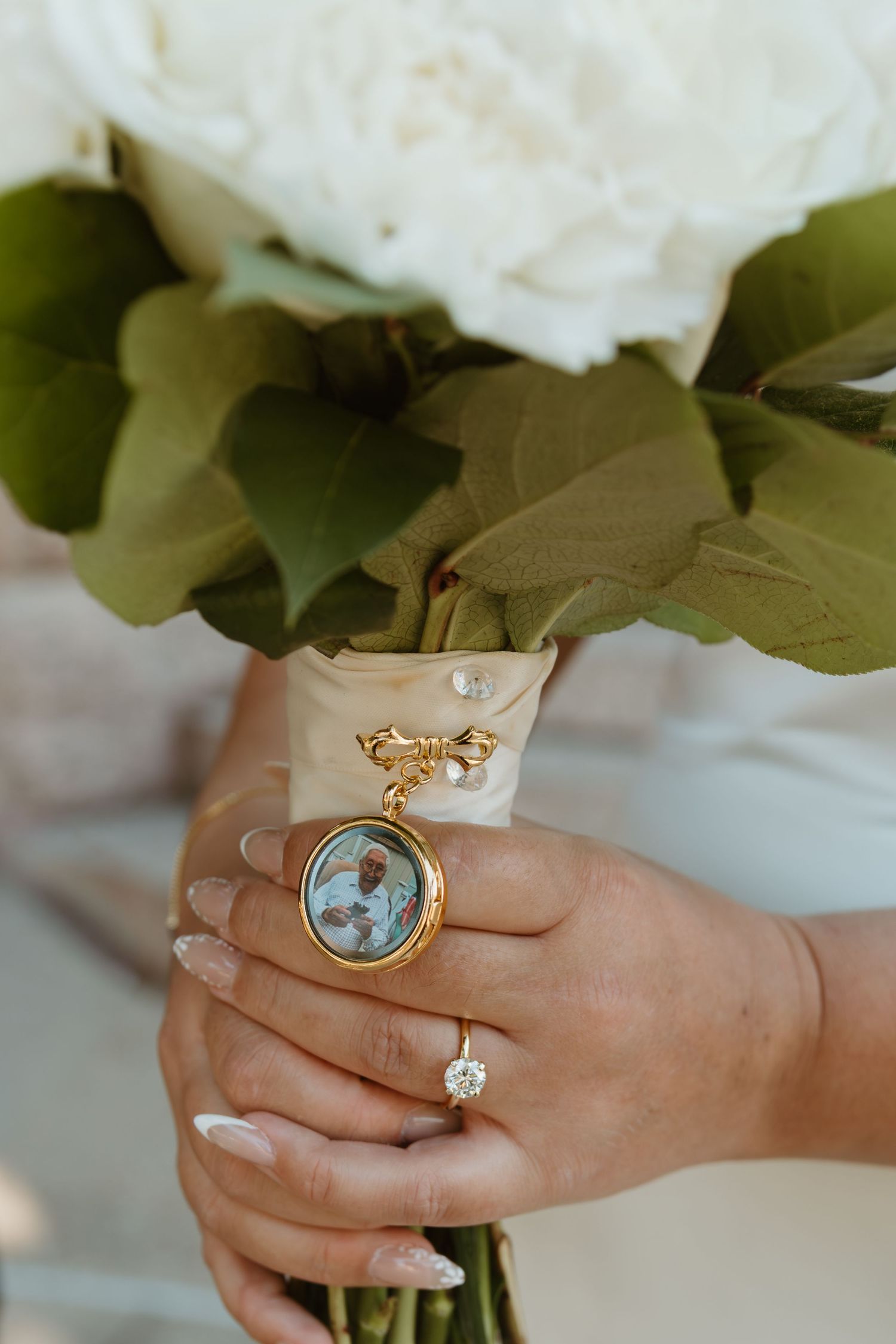 Close-up of hands wearing a vintage locket ring with white flowers in the background. Wedding Photographer DFW