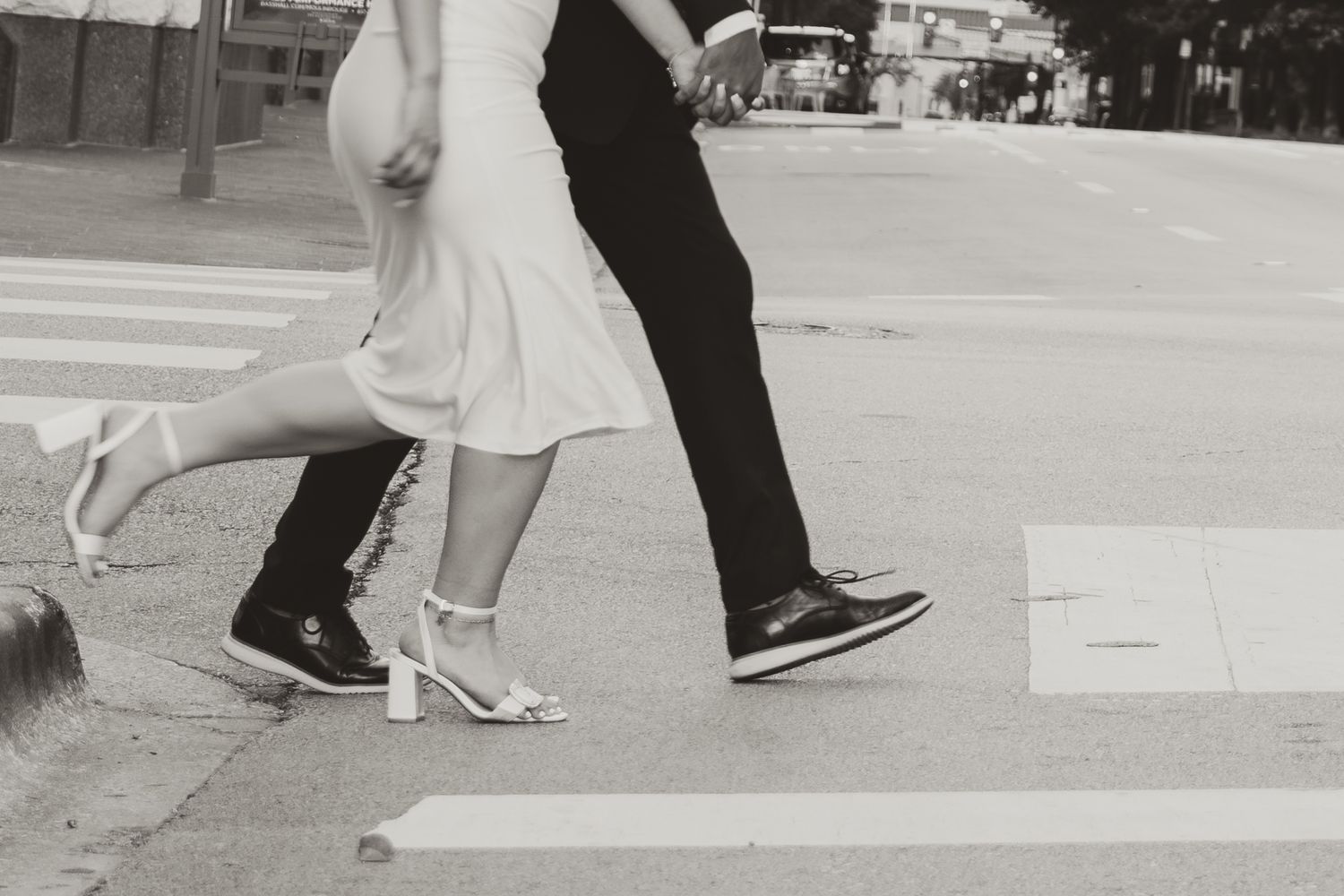 A black and white photo of two sets of feet dancing, one in a white dress and heels, the other in dark pants and shoes.