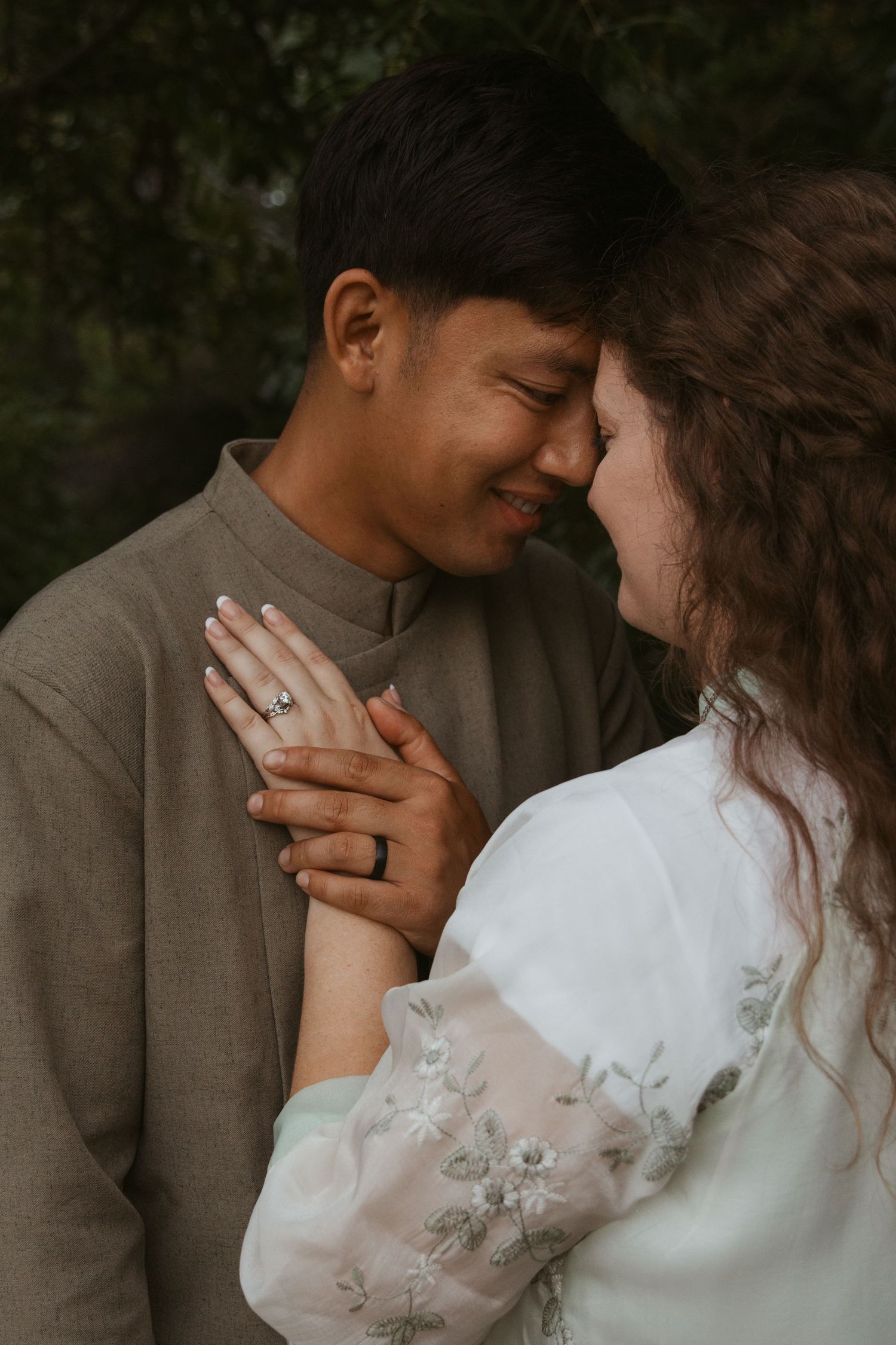 An intimate engagement portrait showing a close embrace and engagement ring.