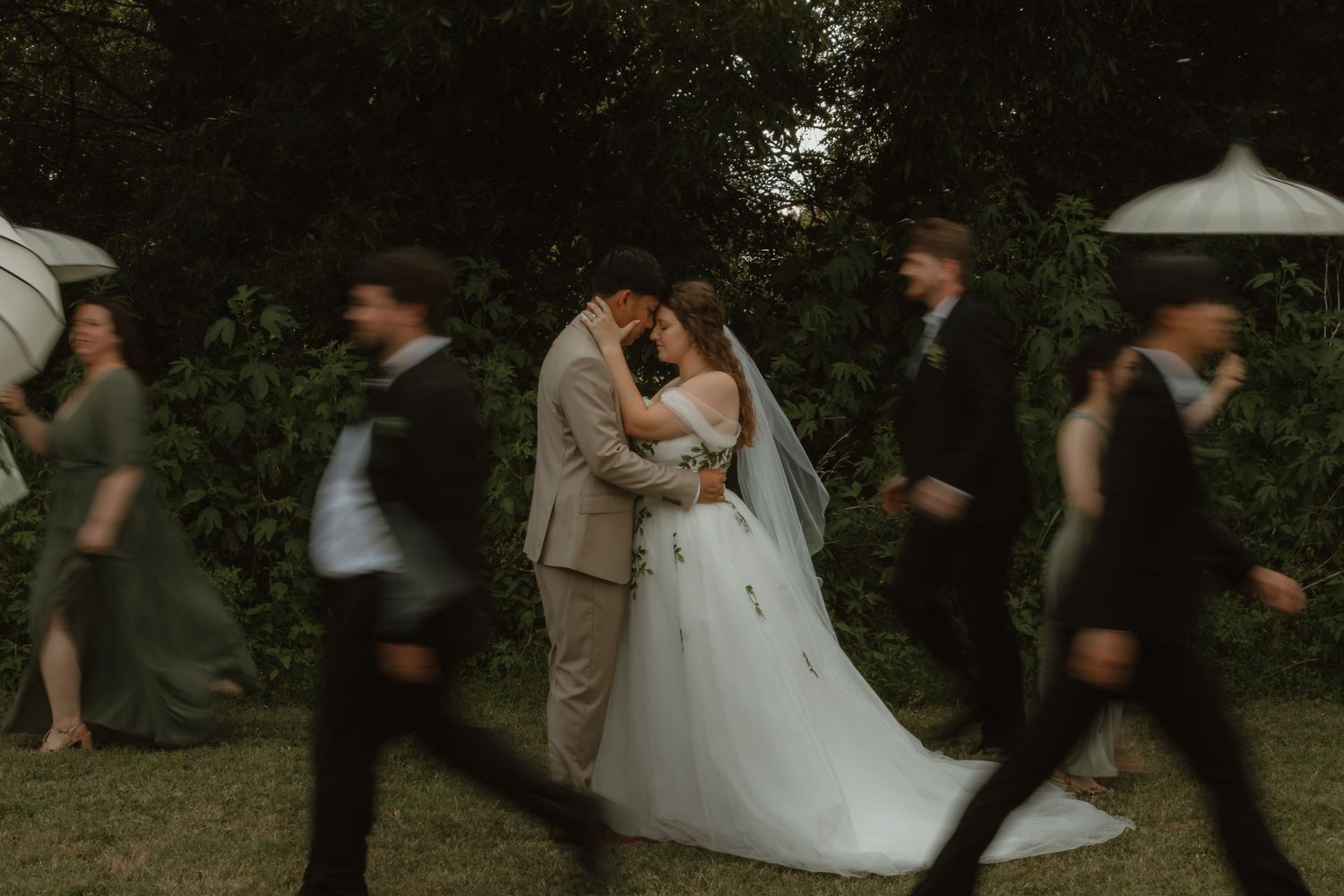 A wedding couple twirls together during their first dance outdoors beneath trees at dusk.