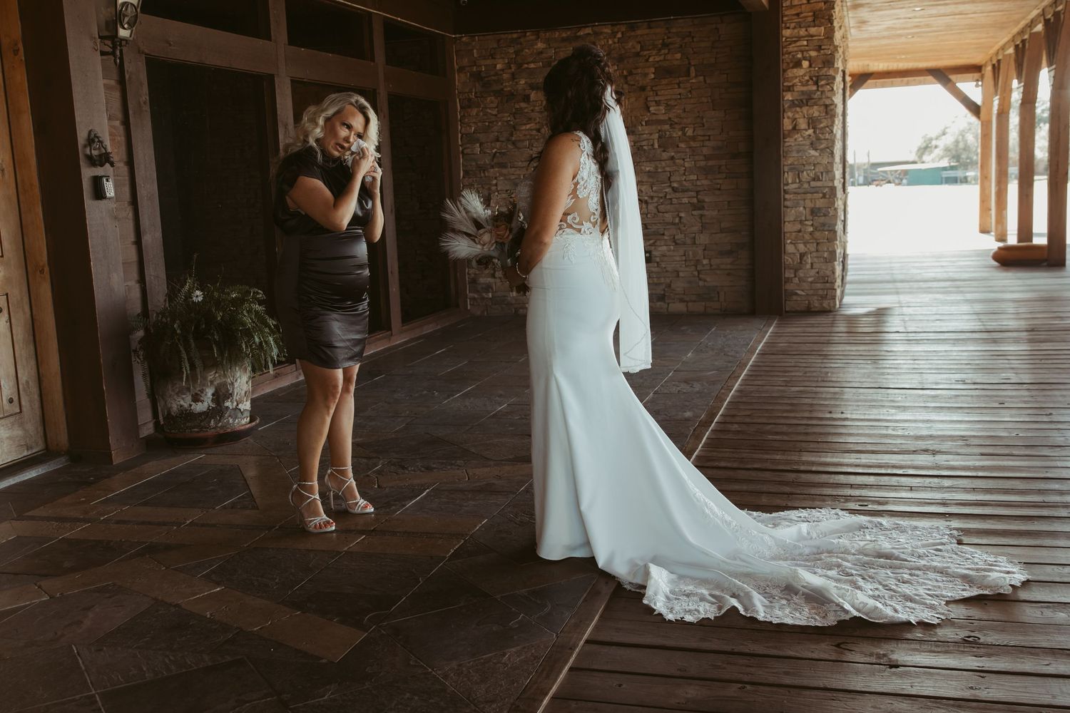 A bride in a flowing white gown with long train standing in a rustic wooden venue. Wedding photographer DFW