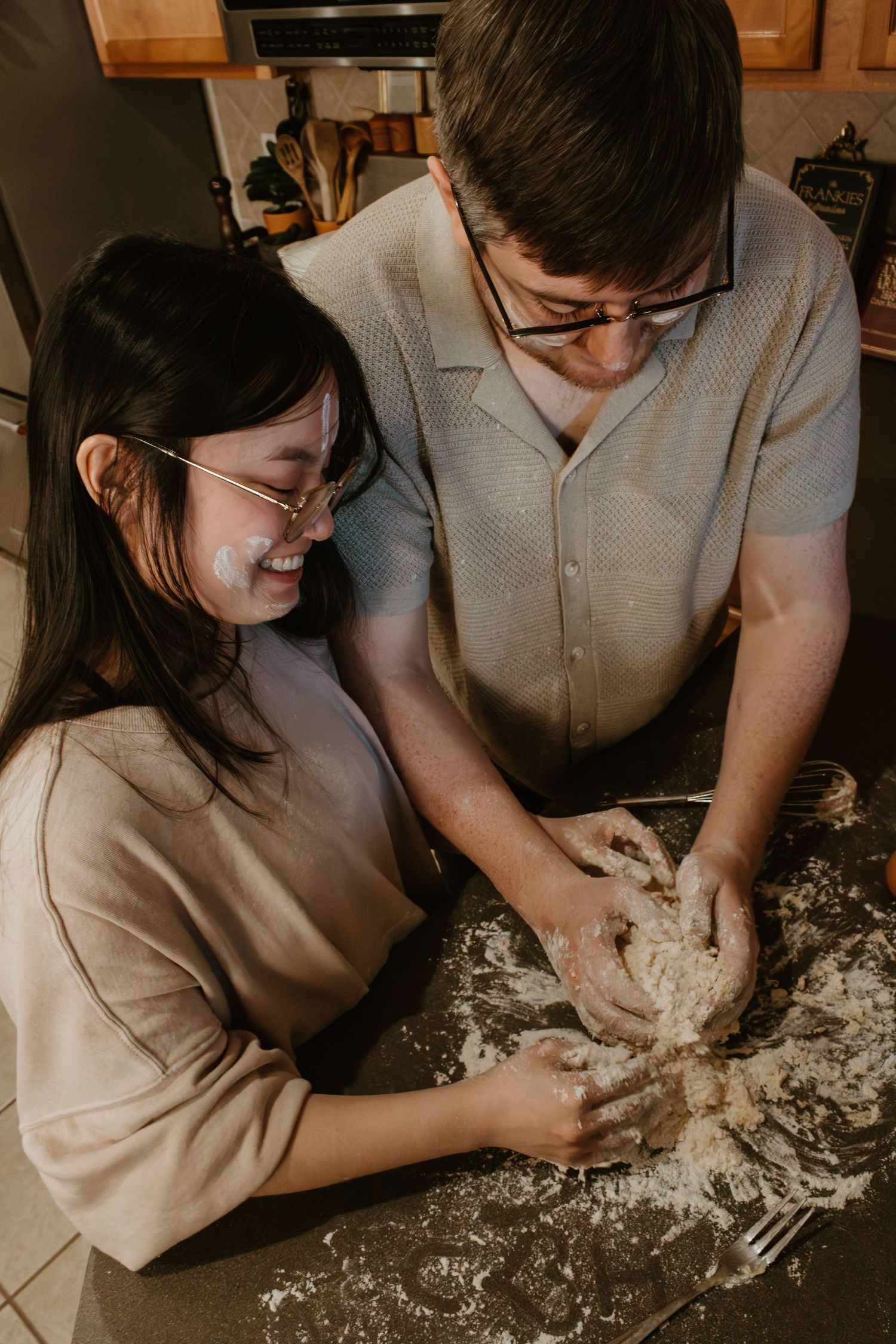 A couple kneading pasta dough together on a flour-covered counter.