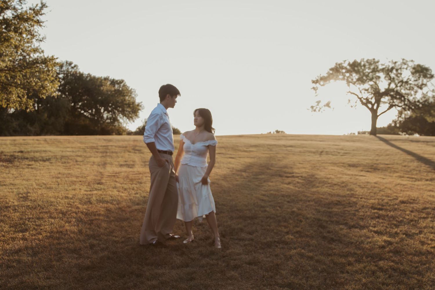 People stand in a dry golden grass field at sunset creating romantic silhouettes.