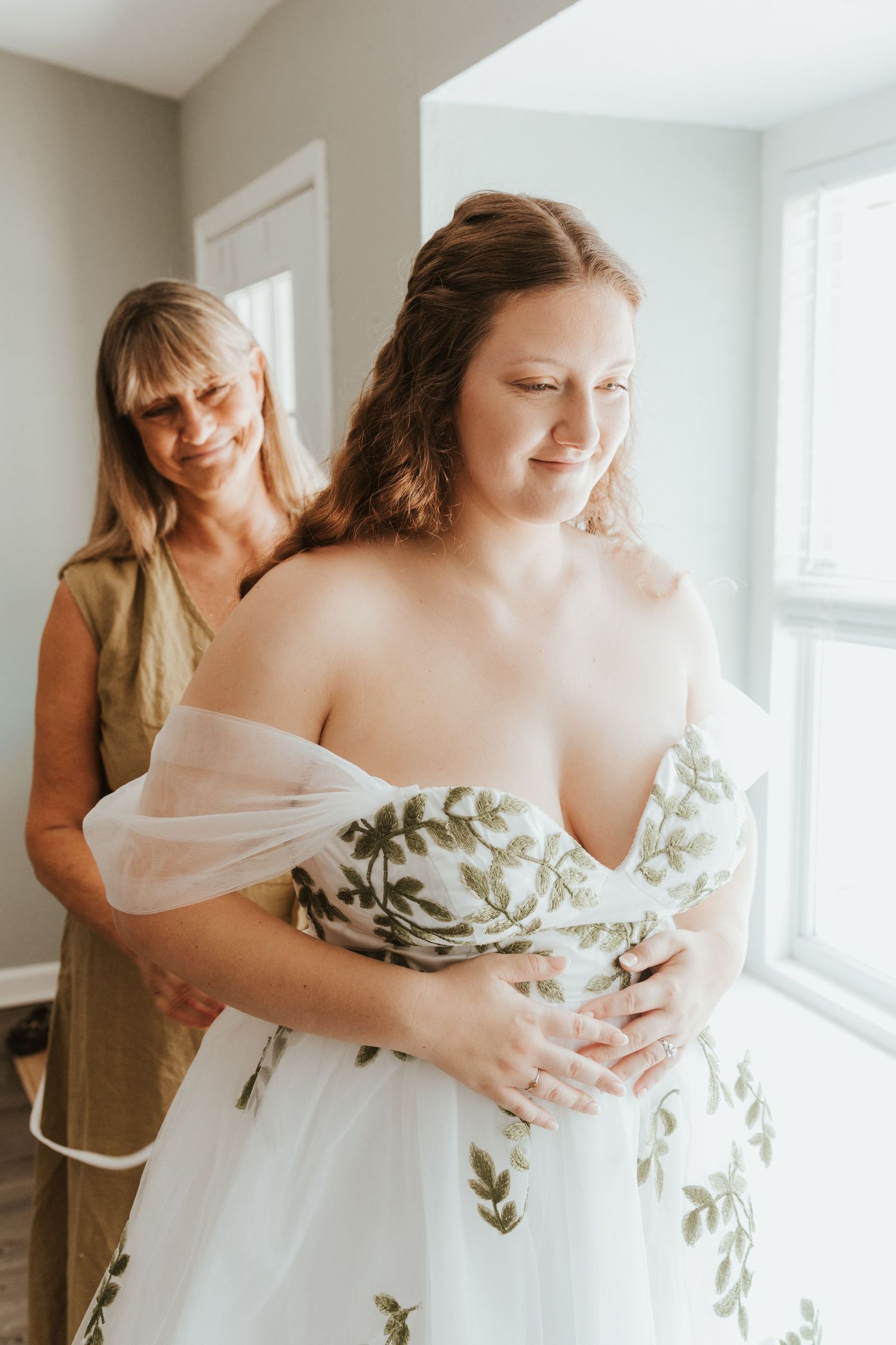 Getting ready scenes of a bride being helped into her white wedding gown with floral details.