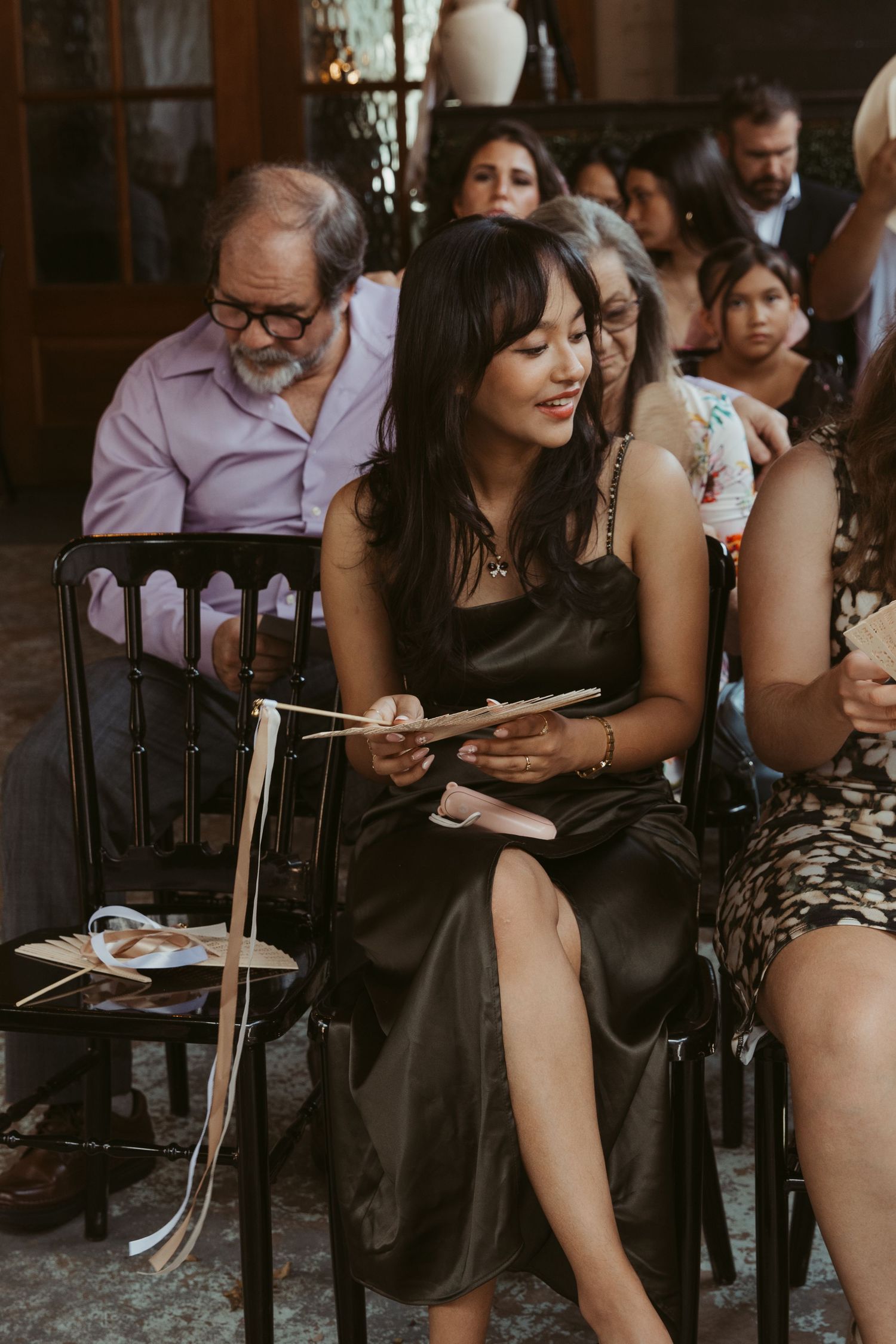 Wedding guests seated in dark chairs during an indoor ceremony.