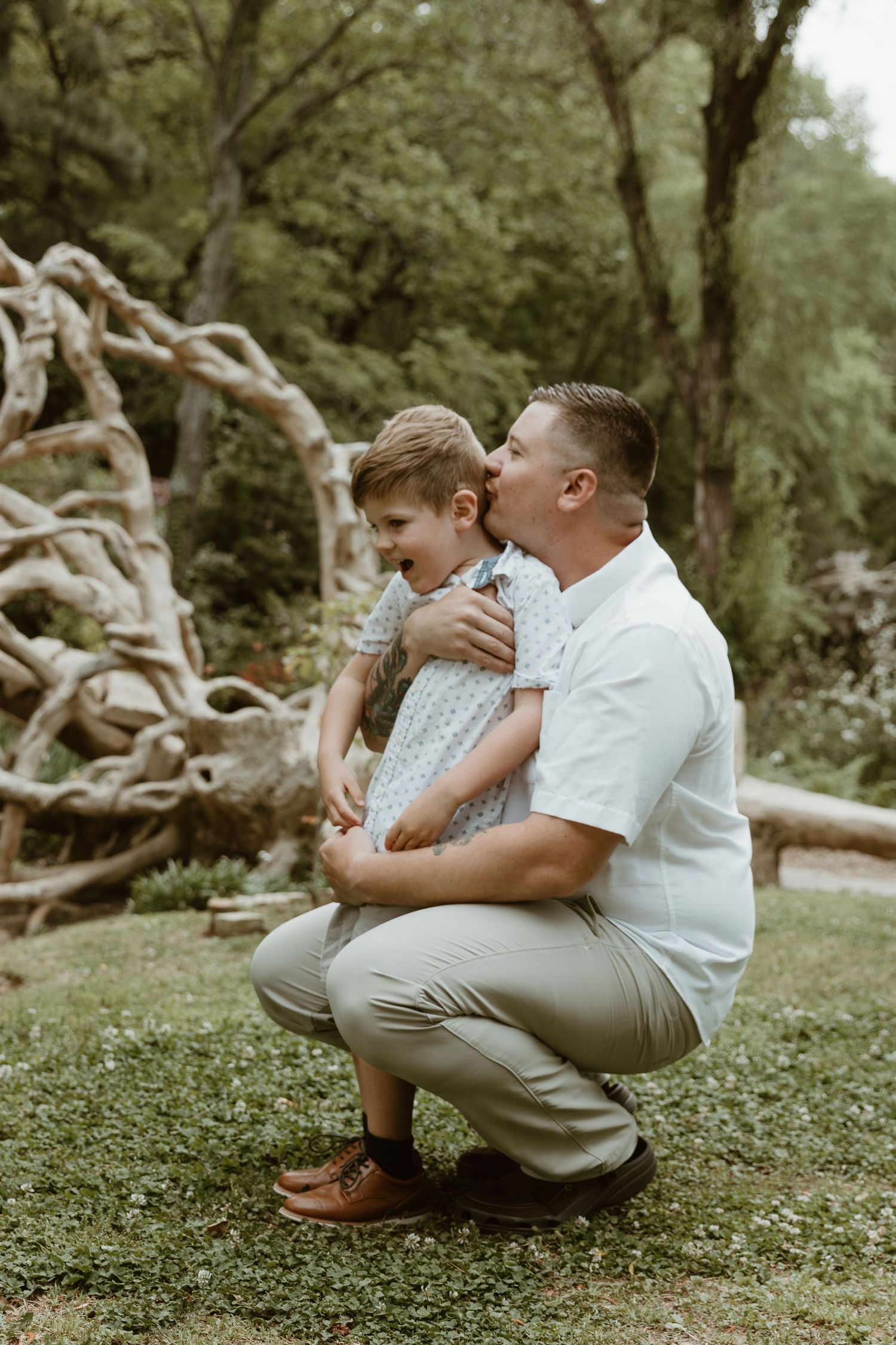 A tender moment between parent and child kneeling together in a wooded outdoor setting.
